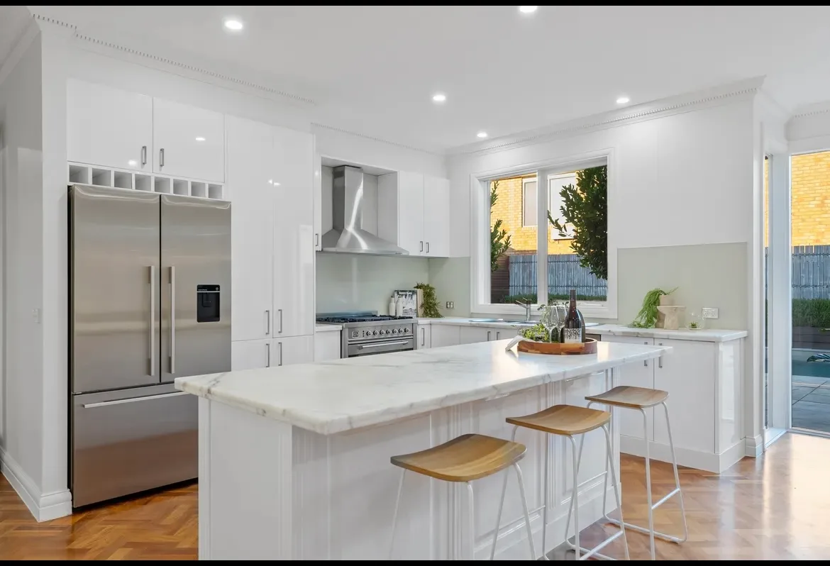 Kitchen with white resurfaced cabinetry, stone island bench and stainless steel appliances