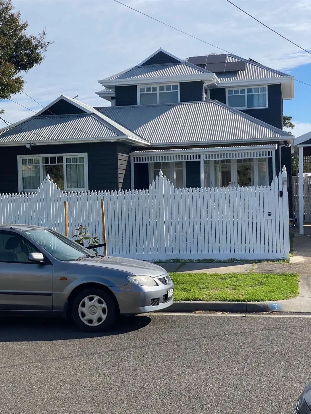 Navy weatherboard home with white picket fence and window trim painted by Jetblack Painting