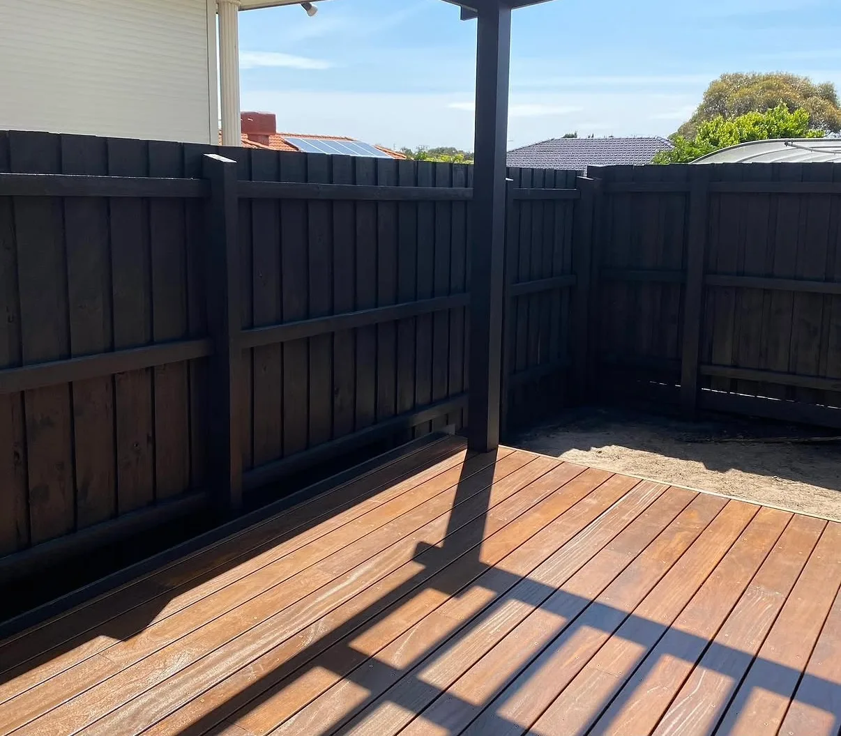 Paling fence painted charcoal black beside a freshly oiled timber deck