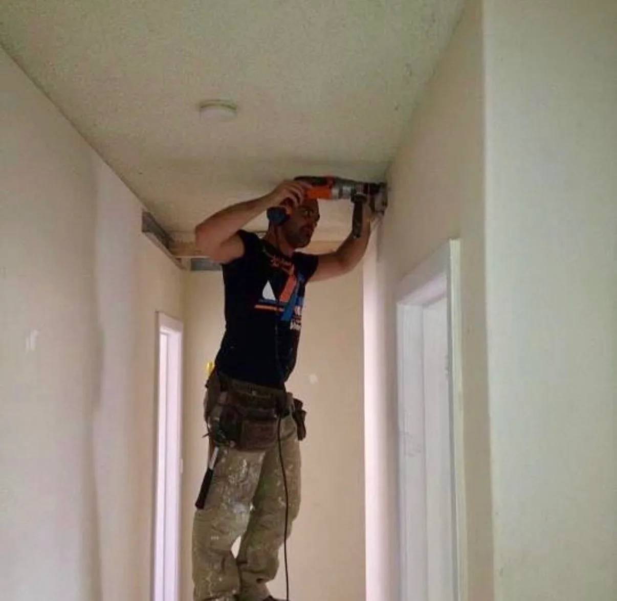 A Jetblack Painting tradesperson on a ladder drilling the ceiling framing while installing a suspended ceiling in an Elsternwick hallway