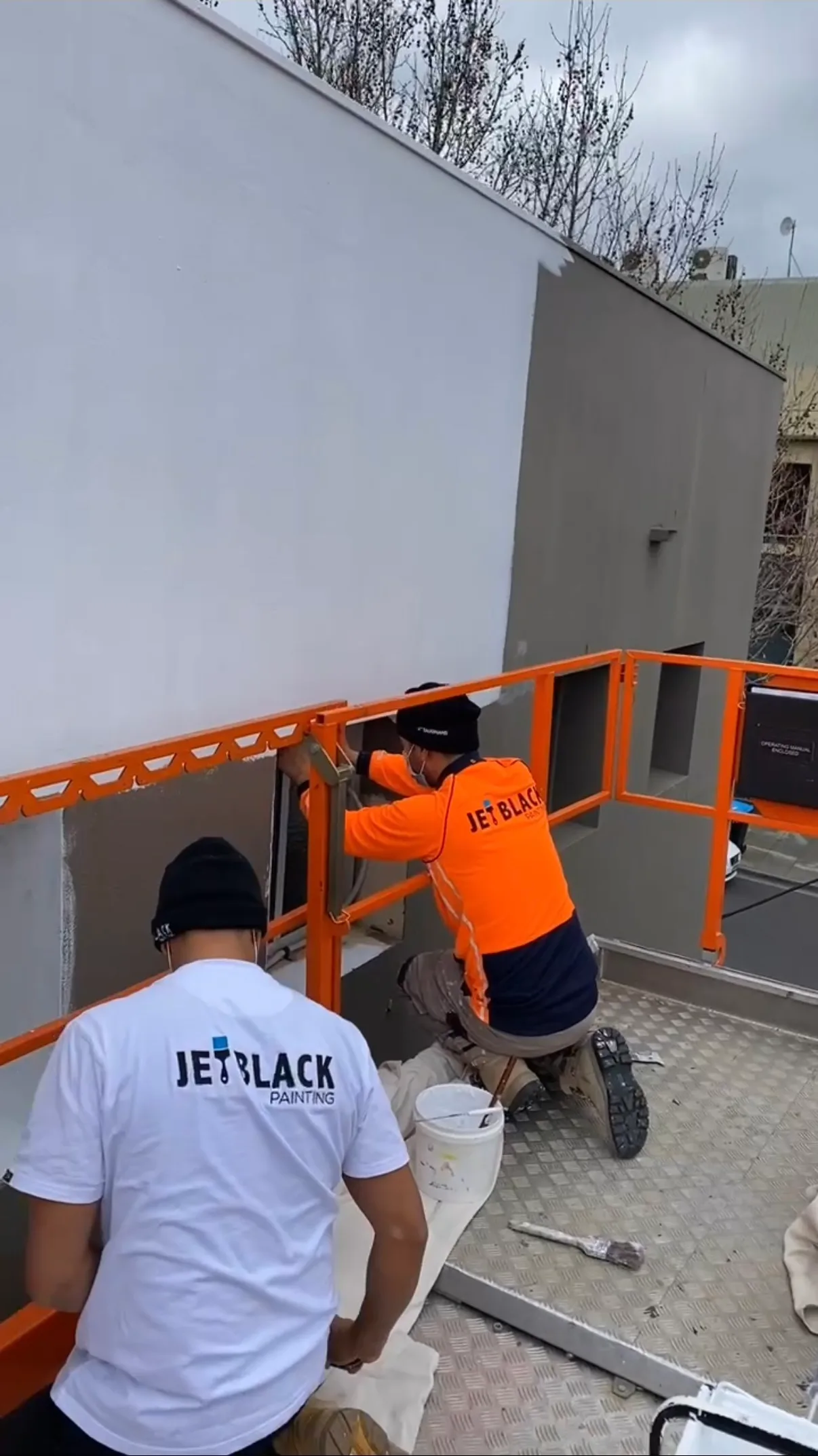 Two Jetblack Painting painters in branded workwear repainting a rendered commercial facade in Armadale from an elevated work platform