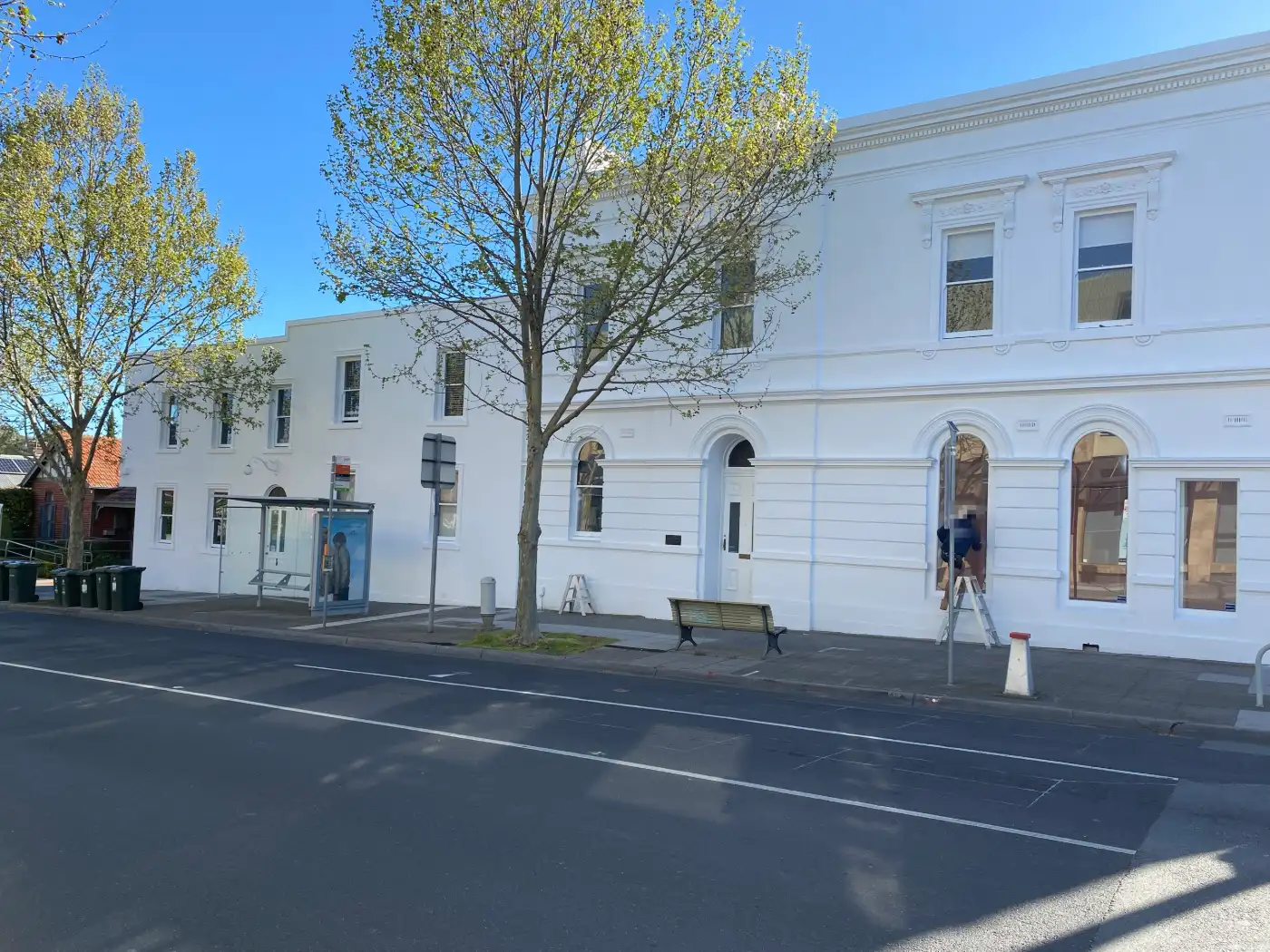 Rendered Italianate commercial building on High Street, Armadale, repainted white, with arched ground-floor windows, a dentilled cornice and a stepped parapet above the footpath
