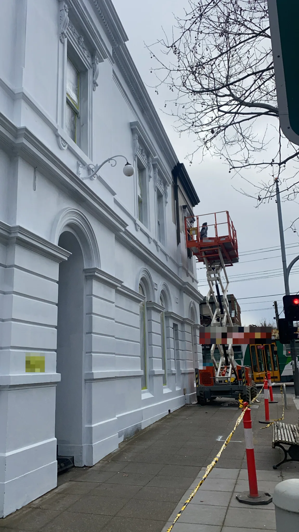 A heritage commercial building in Armadale being repainted white from a scissor lift, with ornate cornice and window mouldings and arched ground-floor windows