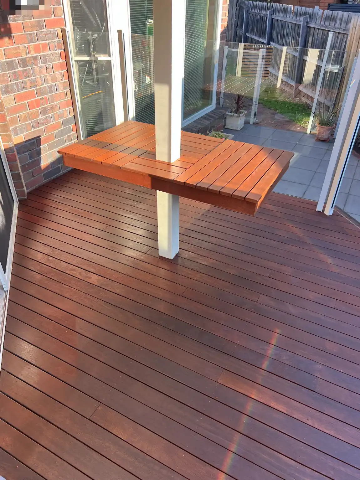 Rear hardwood deck at a Aspendale Gardens home finished in deep red-brown, with a timber bench built around a white verandah post beside glass fencing