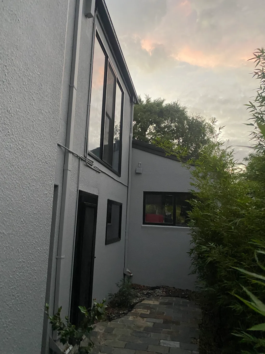 Side path of a rendered home in Balwyn after exterior painting, with light grey walls and pipework and black-framed windows and door