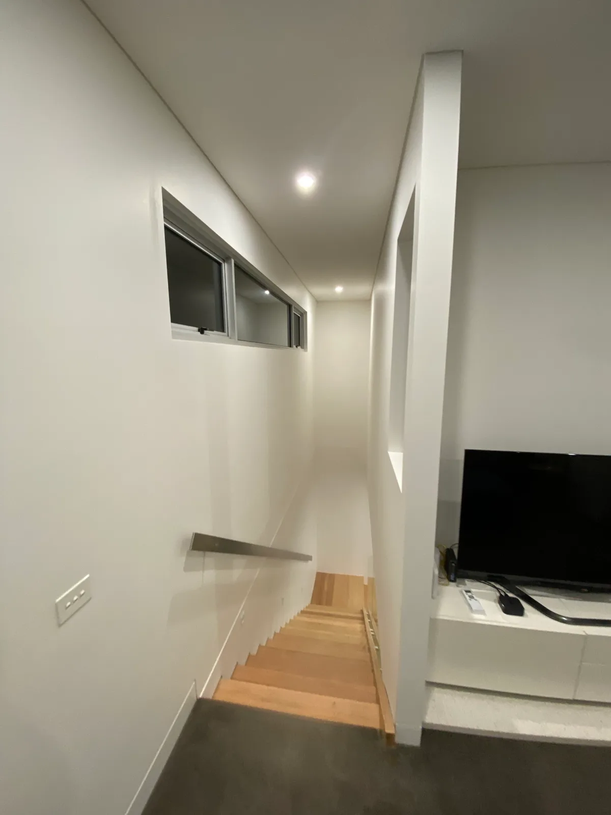 Finished stairwell in a Beaumaris home seen from the top step, white walls and ceiling with a stainless handrail, high window and timber stair treads
