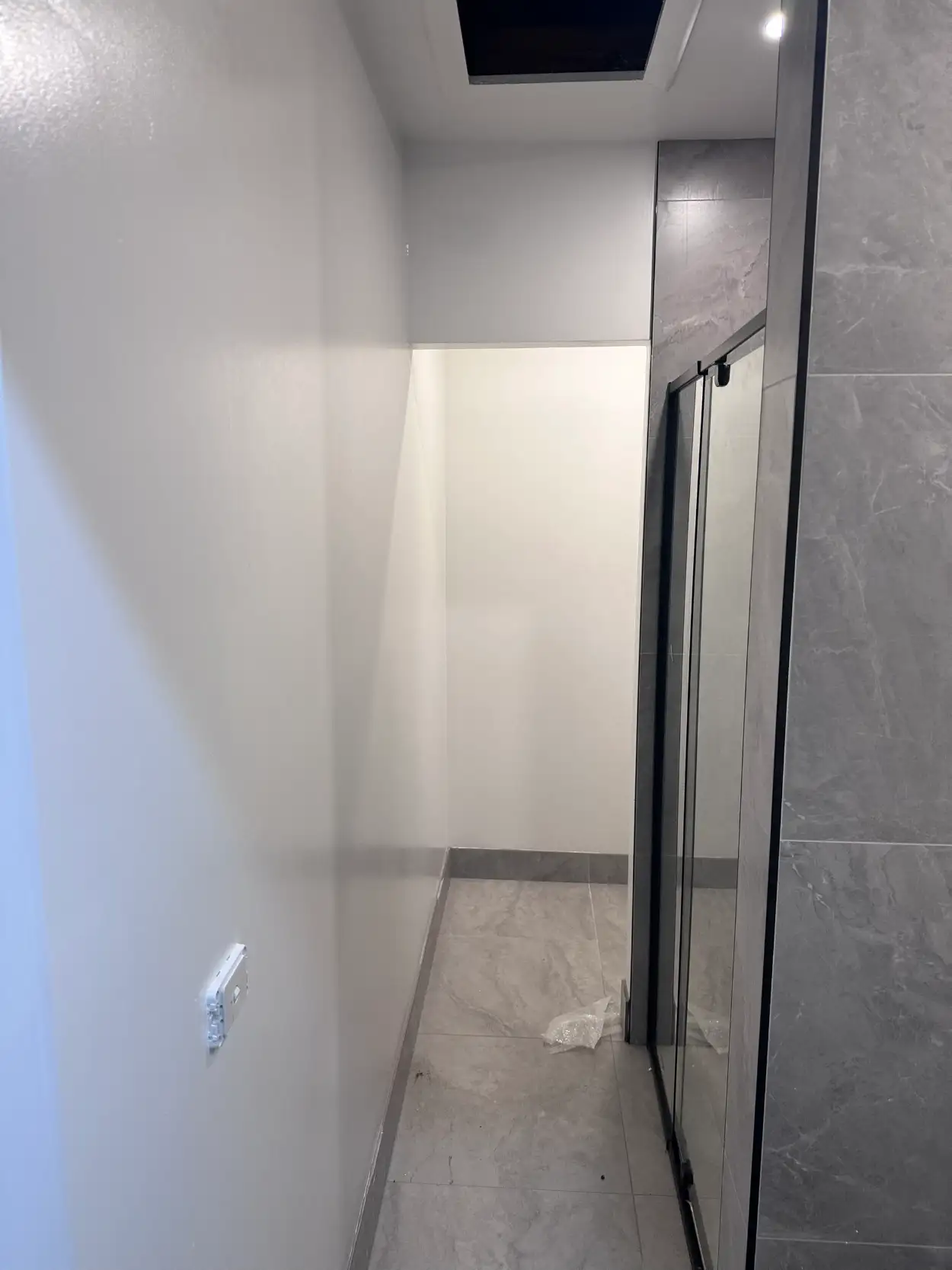 White walls and ceiling in a renovated Bentleigh bathroom, with a recess under a bulkhead beside the tiled shower and a grey tiled skirting