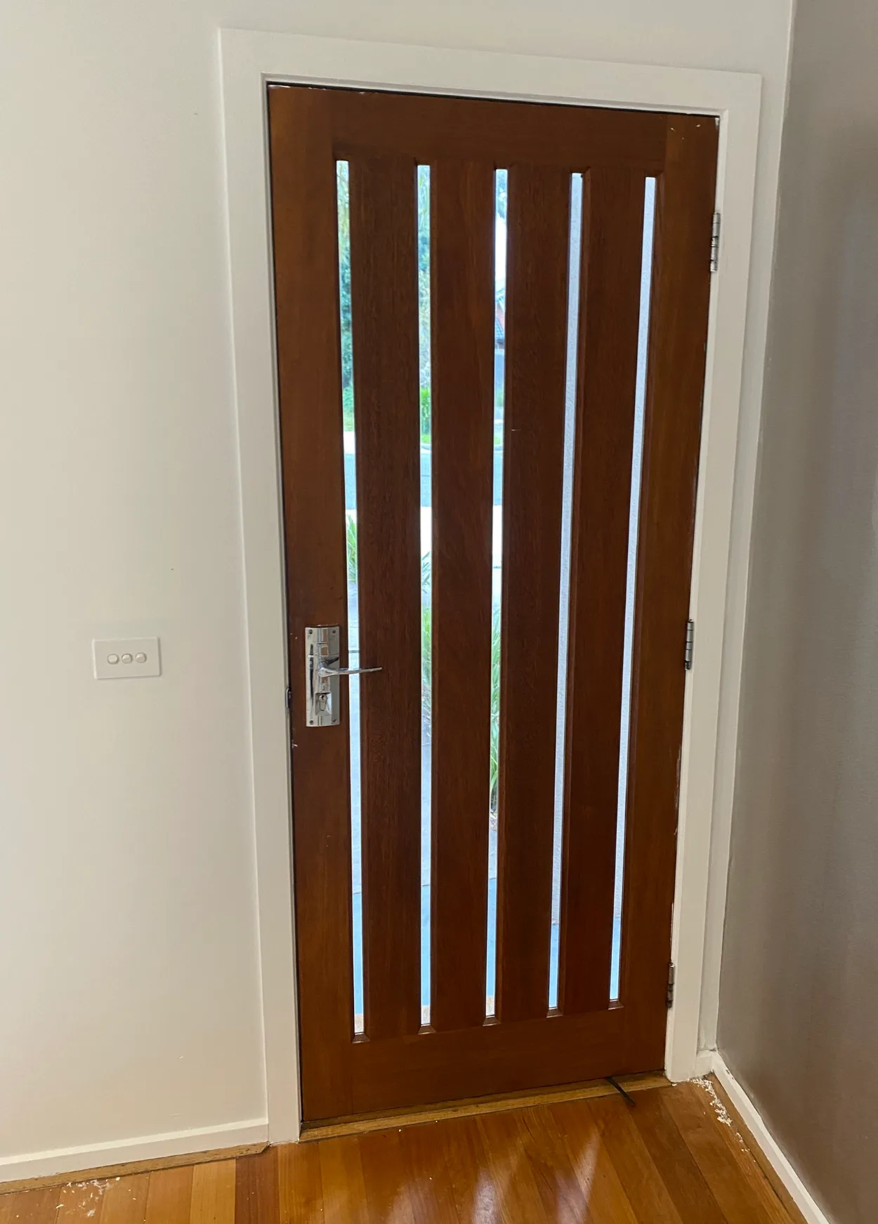 Entry of a Bentleigh East home after interior painting, with white walls, architrave and skirting around a stained timber front door with five vertical glass slots