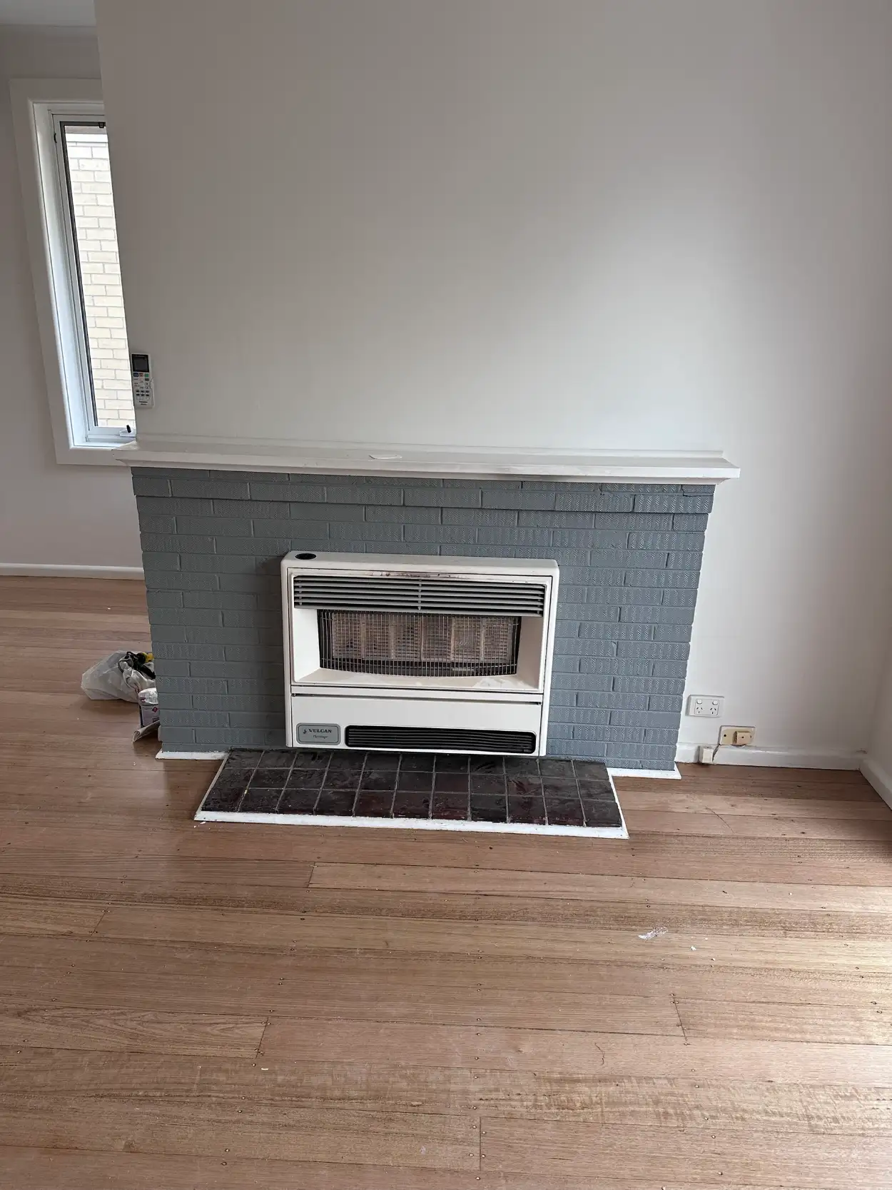 Bentleigh living room after interior painting, with a brick fireplace surround in mid grey, a white mantel shelf and white walls above timber floorboards