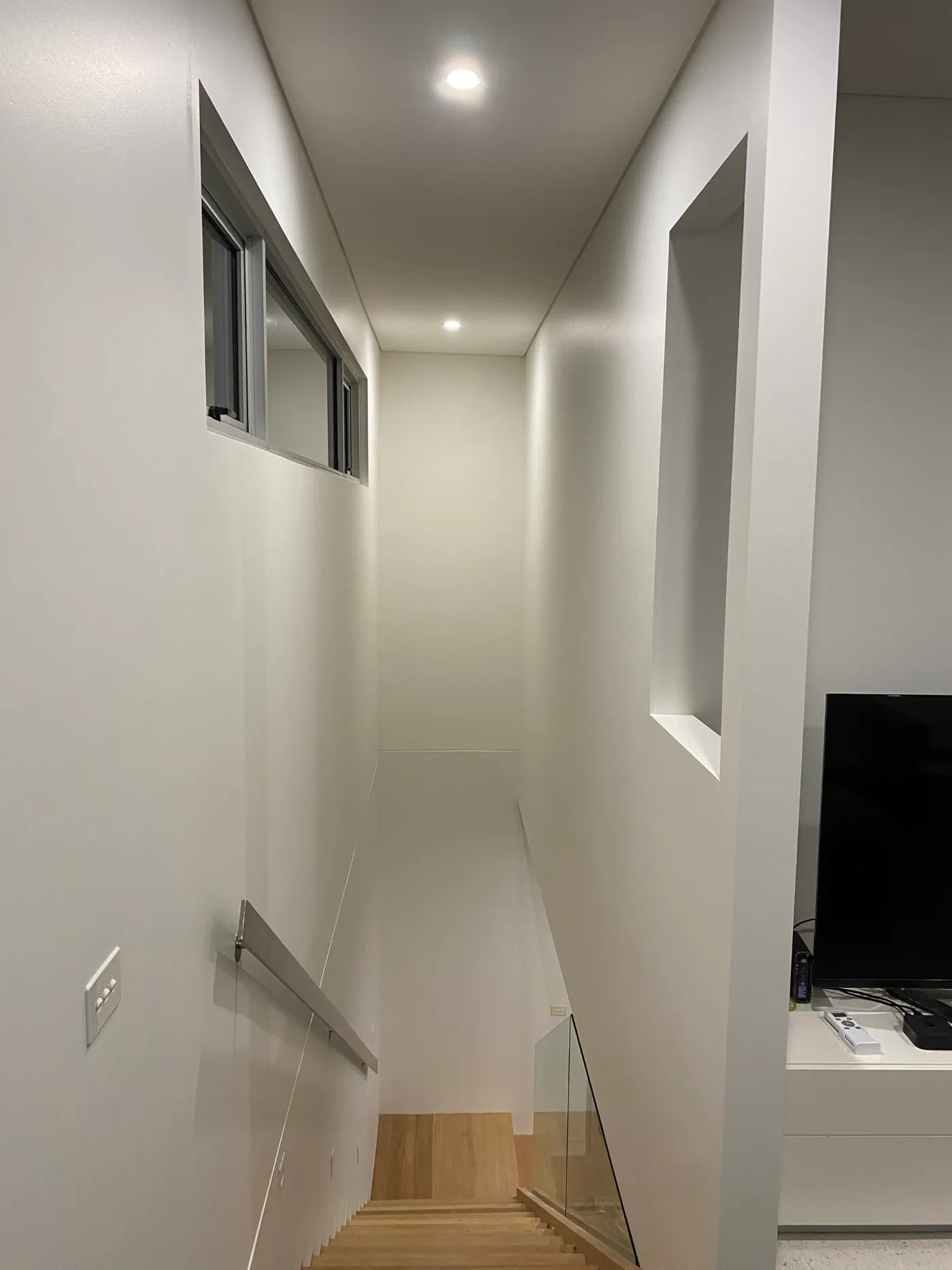 The same Black Rock stairwell void after painting, finished in white with downlights, a glass stair balustrade and timber treads