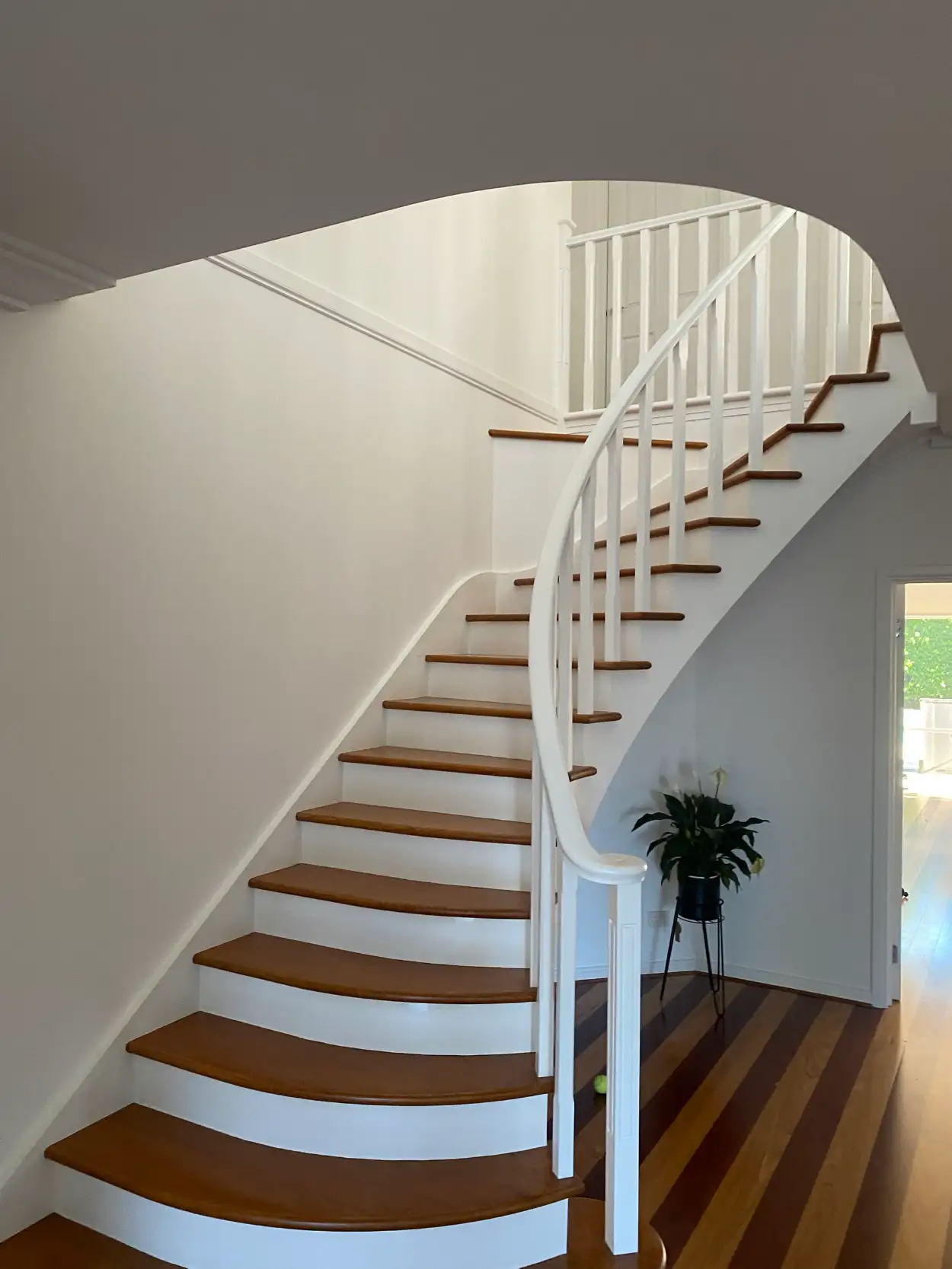 Curved staircase in a Brighton home after an interior repaint, with white risers, stringer, balusters and handrail against timber treads and two-tone floorboards
