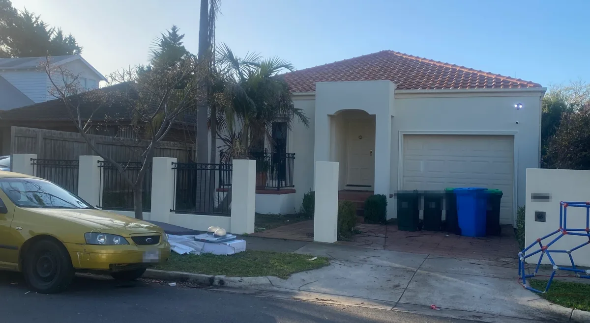 Front of a single-storey rendered Brighton East home in cream with an arched entry portico, a cream garage door and a matching rendered front fence with black metal panels