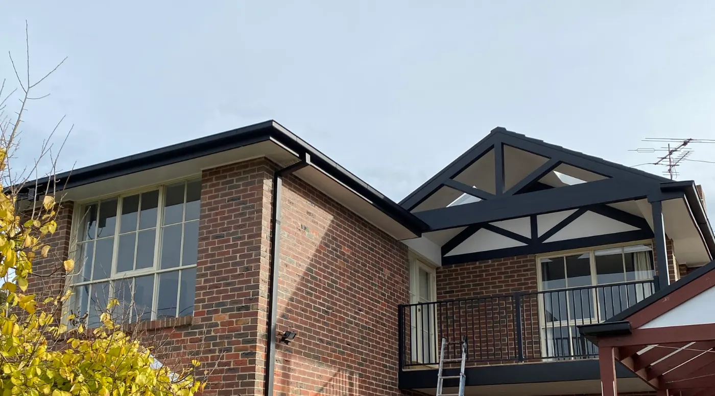 Two-storey red brick Brighton East home after exterior painting, with decorative gable trusses, fascia and gutter in dark charcoal against off-white gable infill