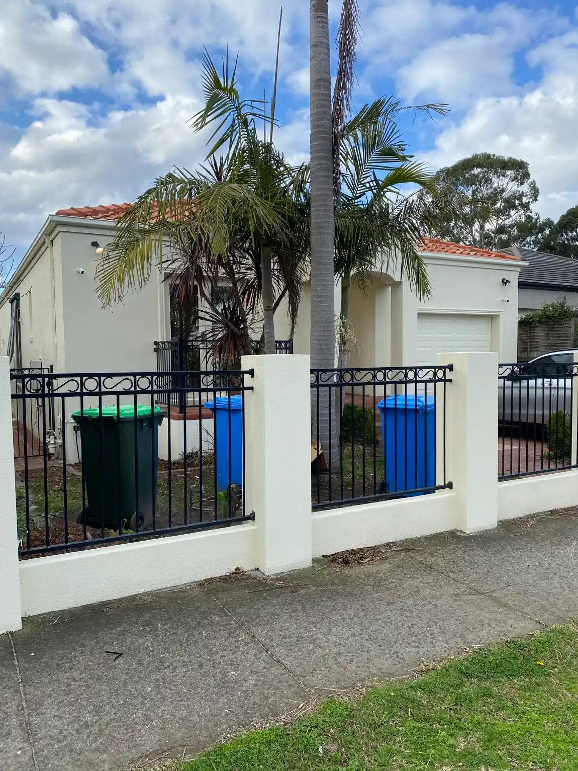 Single-storey rendered Brighton East home and its rendered front fence, both in cream, with black metal fence panels between the pillars