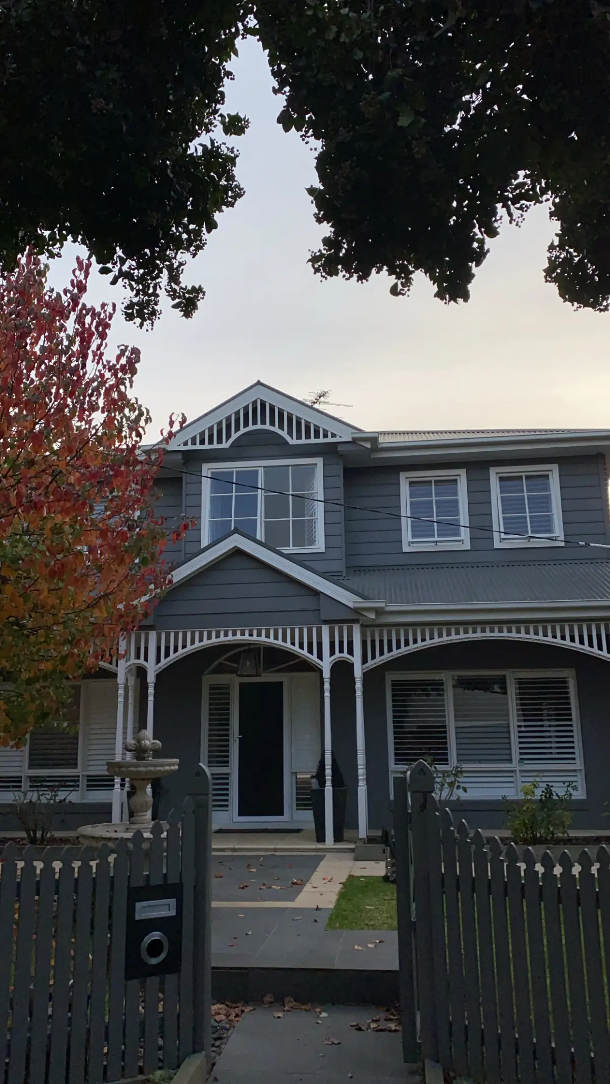 Brighton weatherboard home after repainting, in dark charcoal with white fretwork, verandah posts and window frames