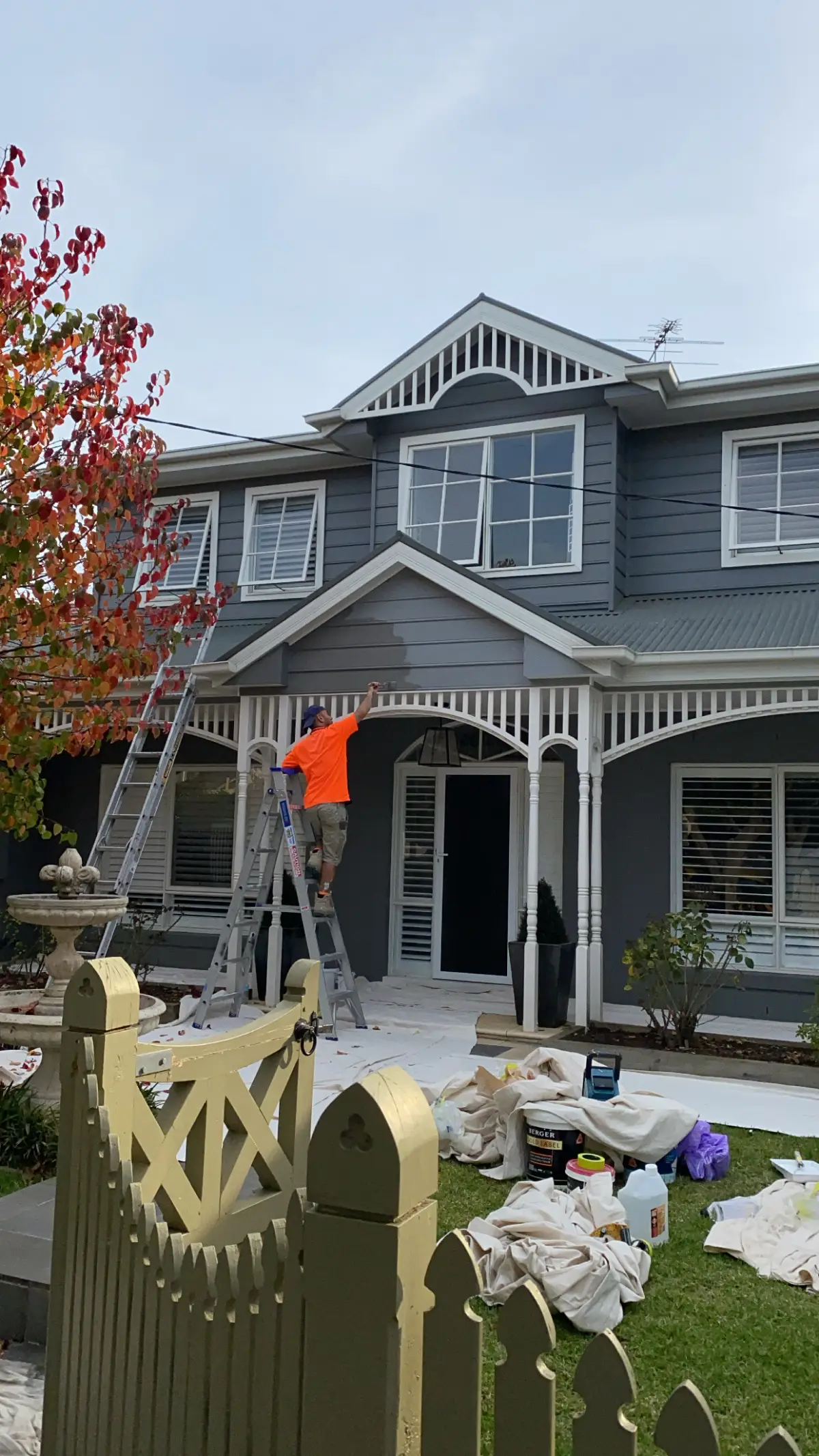 A painter on a ladder cutting in the verandah fretwork by brush during a Brighton exterior repaint