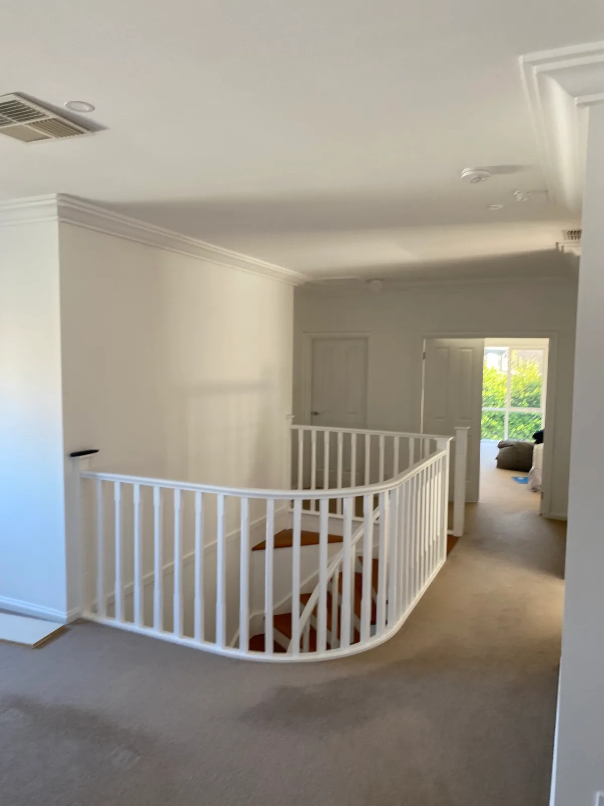 Upstairs landing and hall of a Brighton home after an interior repaint, with a curved white balustrade around the stairwell, white walls, cornices and panel doors, and timber stair treads visible through the balusters