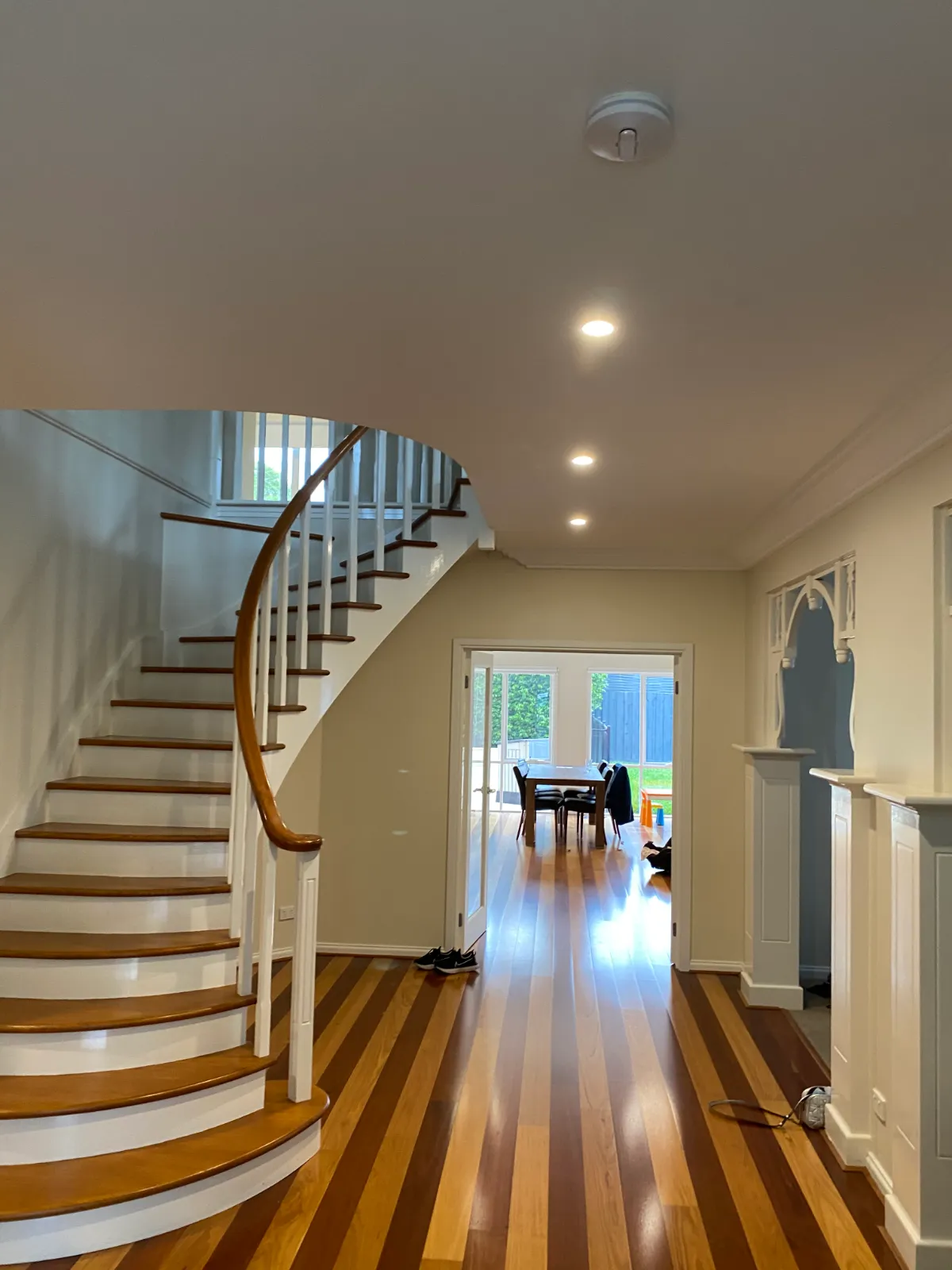 Finished stair hall in a Brighton home after an interior repaint, curved staircase with white risers and balusters against timber treads, handrail and floorboards
