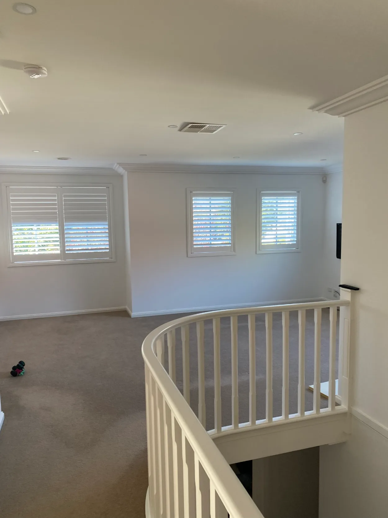 Upstairs landing in a Brighton home after an interior repaint, white walls, ceiling and cornice above a curved white balustrade around the stair void