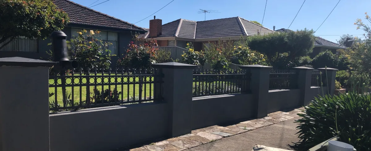 The same Burwood rendered fence near Box Hill seen along the footpath, charcoal pillars and walls with black metal infill panels
