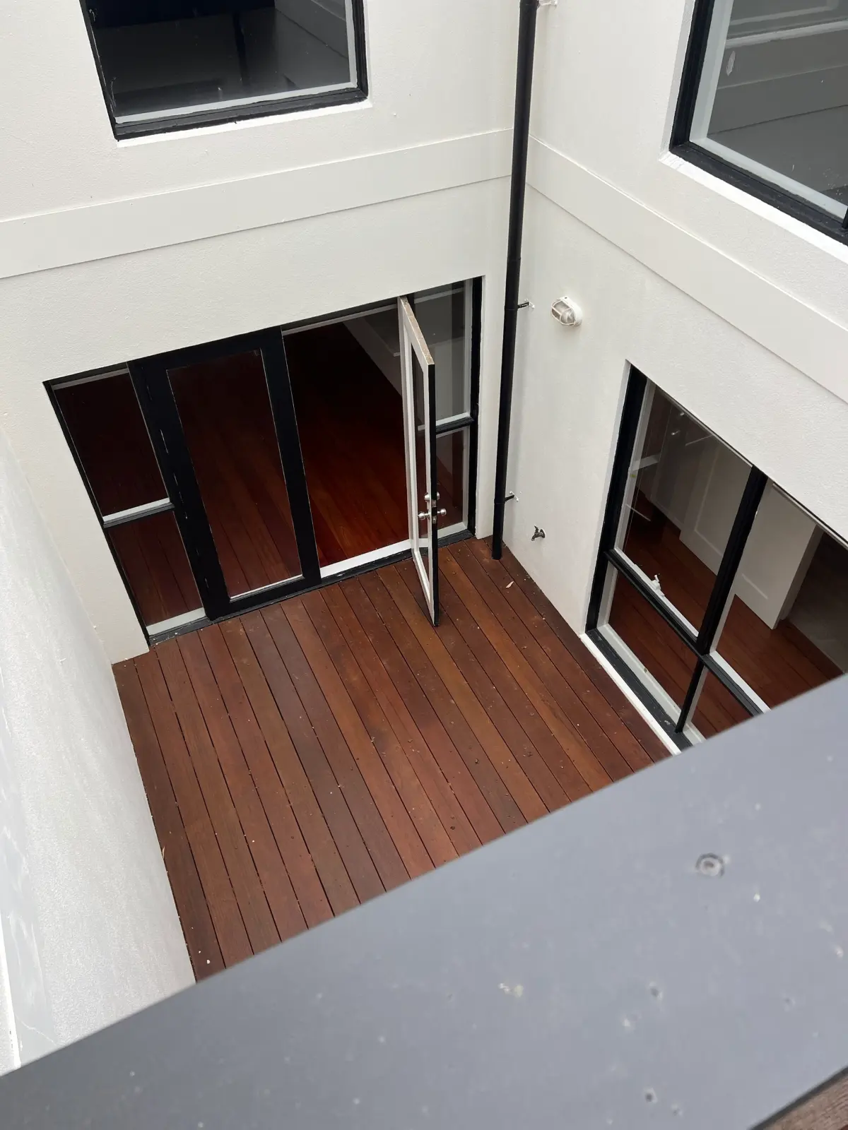 Looking down from an upper balcony into the white rendered internal courtyard of a Carlton townhouse, with black-framed doors and windows around a timber deck