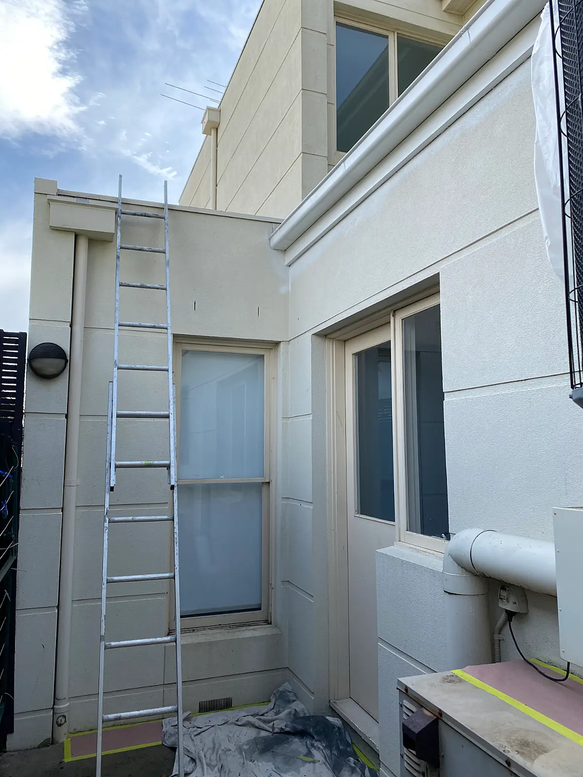 Drop sheets, ladder and masking tape in place on Caulfield eaves and rendered wall before painting
