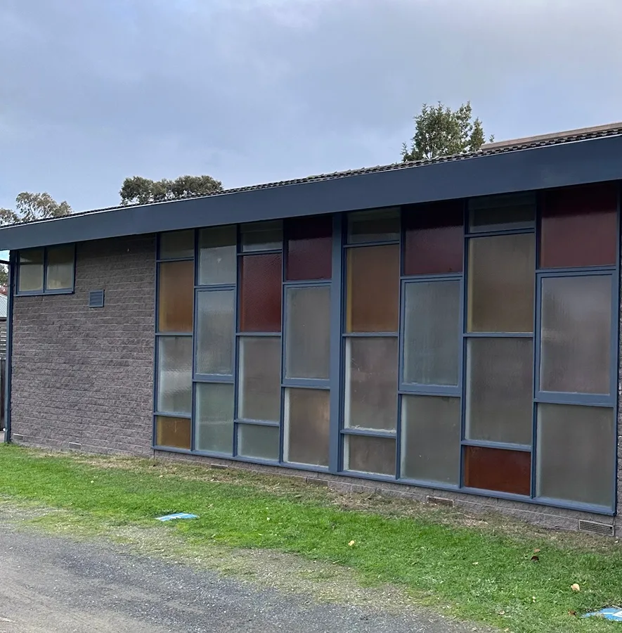 Brick community building in Cheltenham after exterior painting, with a deep slate-blue fascia and slate-blue frames around a long wall of coloured and frosted glass panels, and the blockwork unpainted