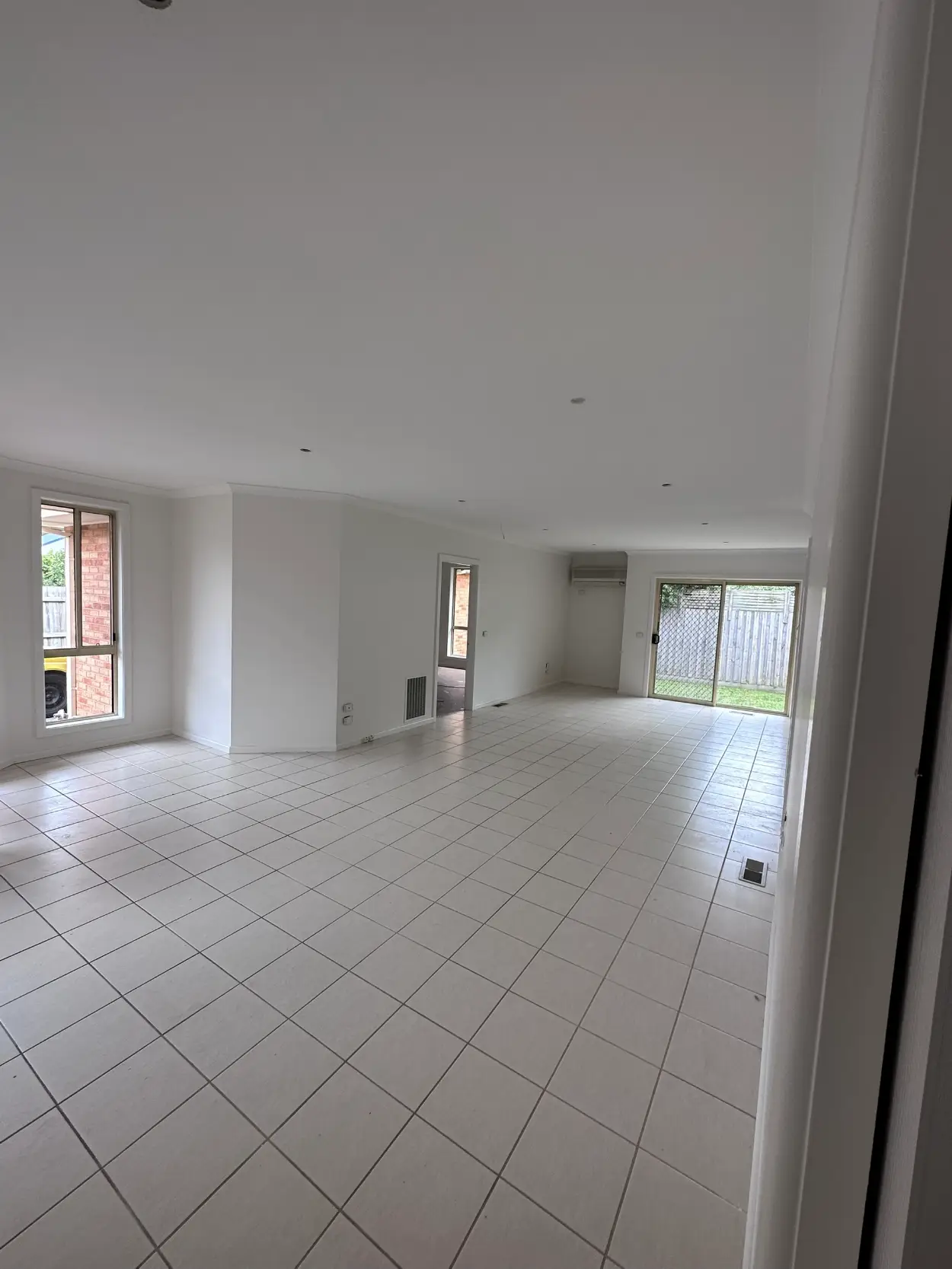 Empty open-plan living and dining area in a Clarinda home after repainting, with white walls and ceiling above a pale tiled floor and a sliding door to the rear yard