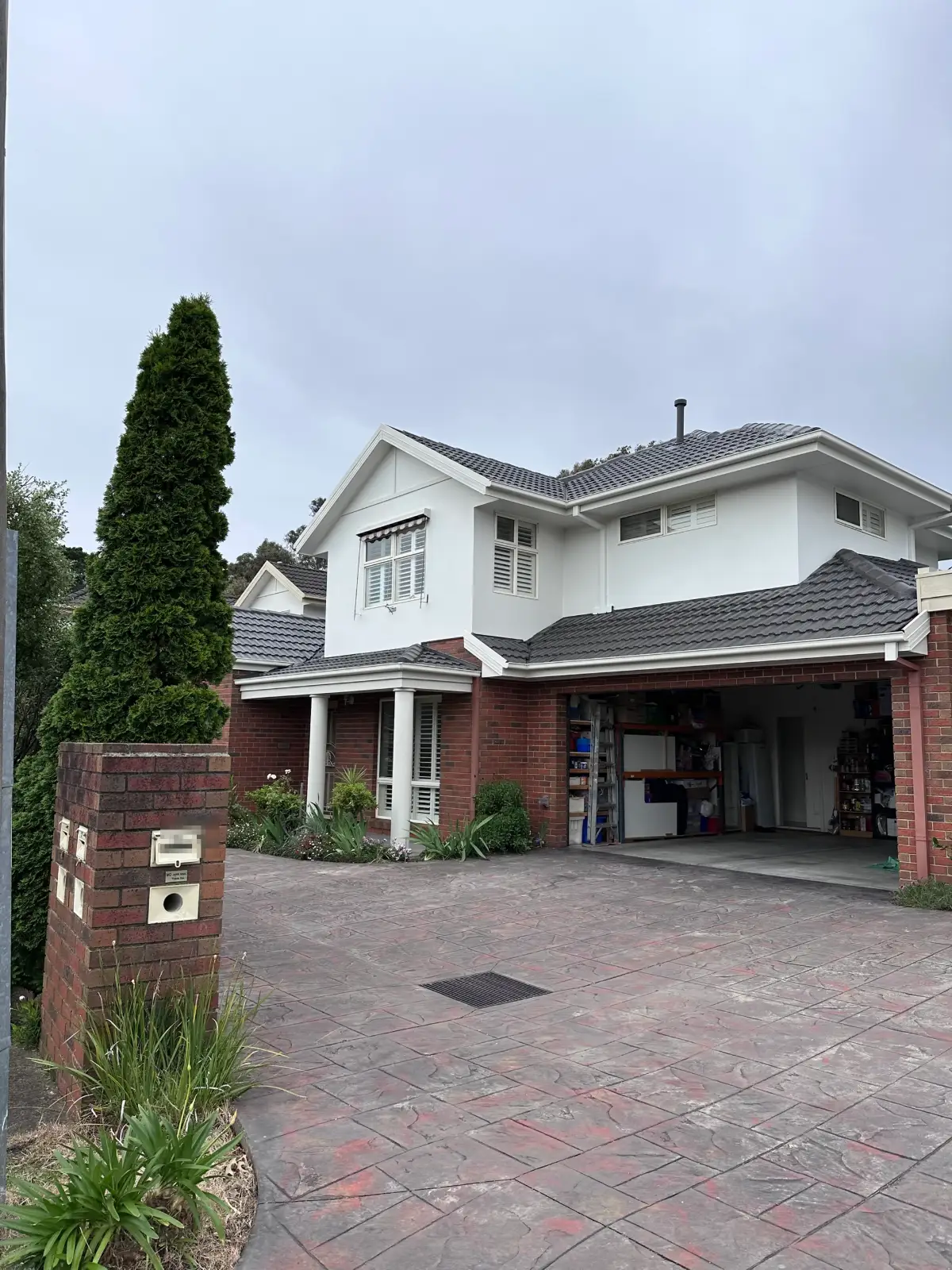 Two-storey Dingley Village home from the driveway after painting, with white rendered upper walls, white fascias and gutters above red brick and a tiled roof