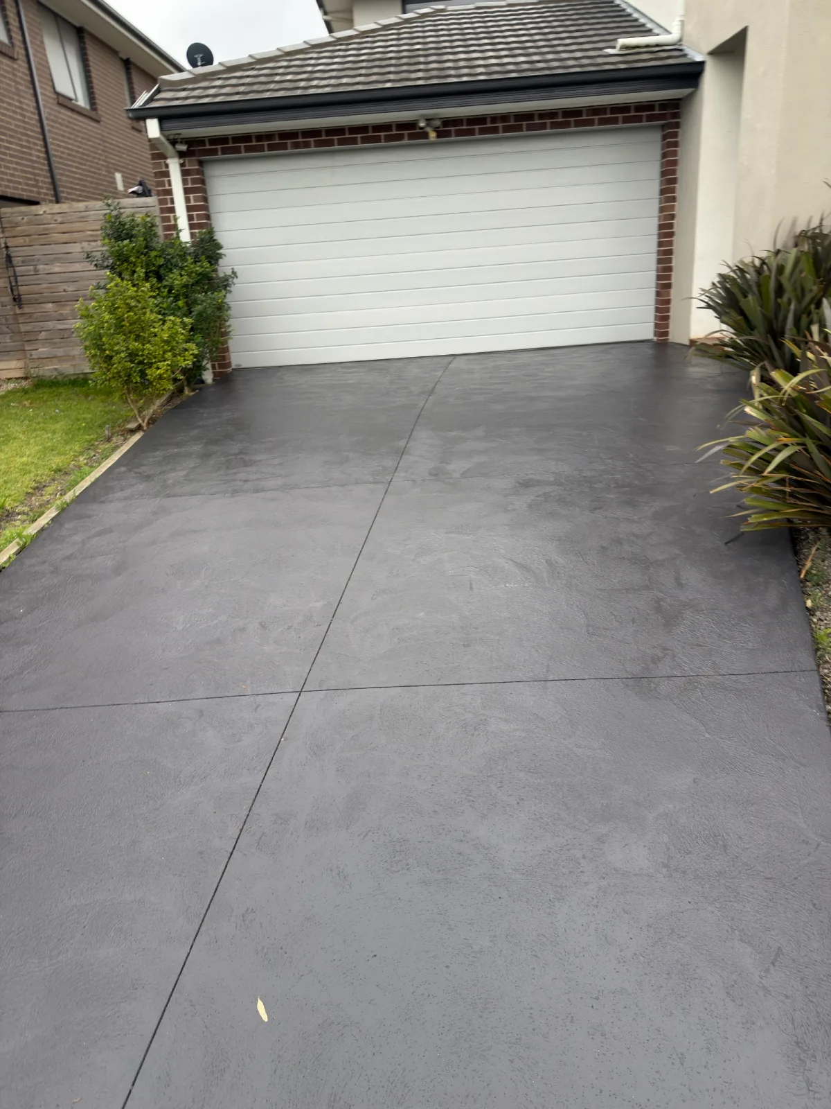 Concrete driveway in Doncaster after coating in charcoal, running up to a white garage door between red brick piers