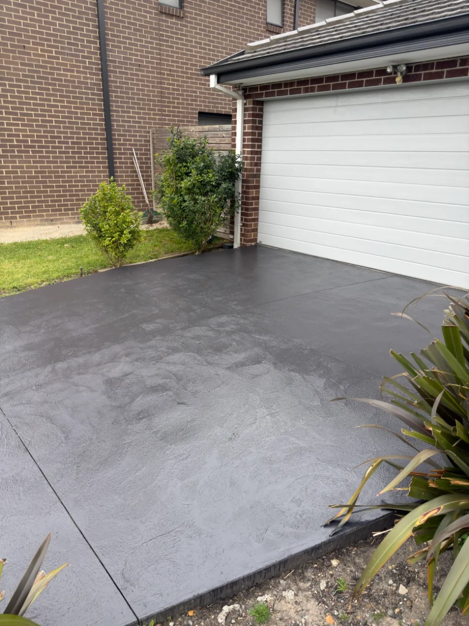 The same charcoal-coated concrete driveway in Doncaster seen from the side, with the coating carried to the slab edge beside the garden bed
