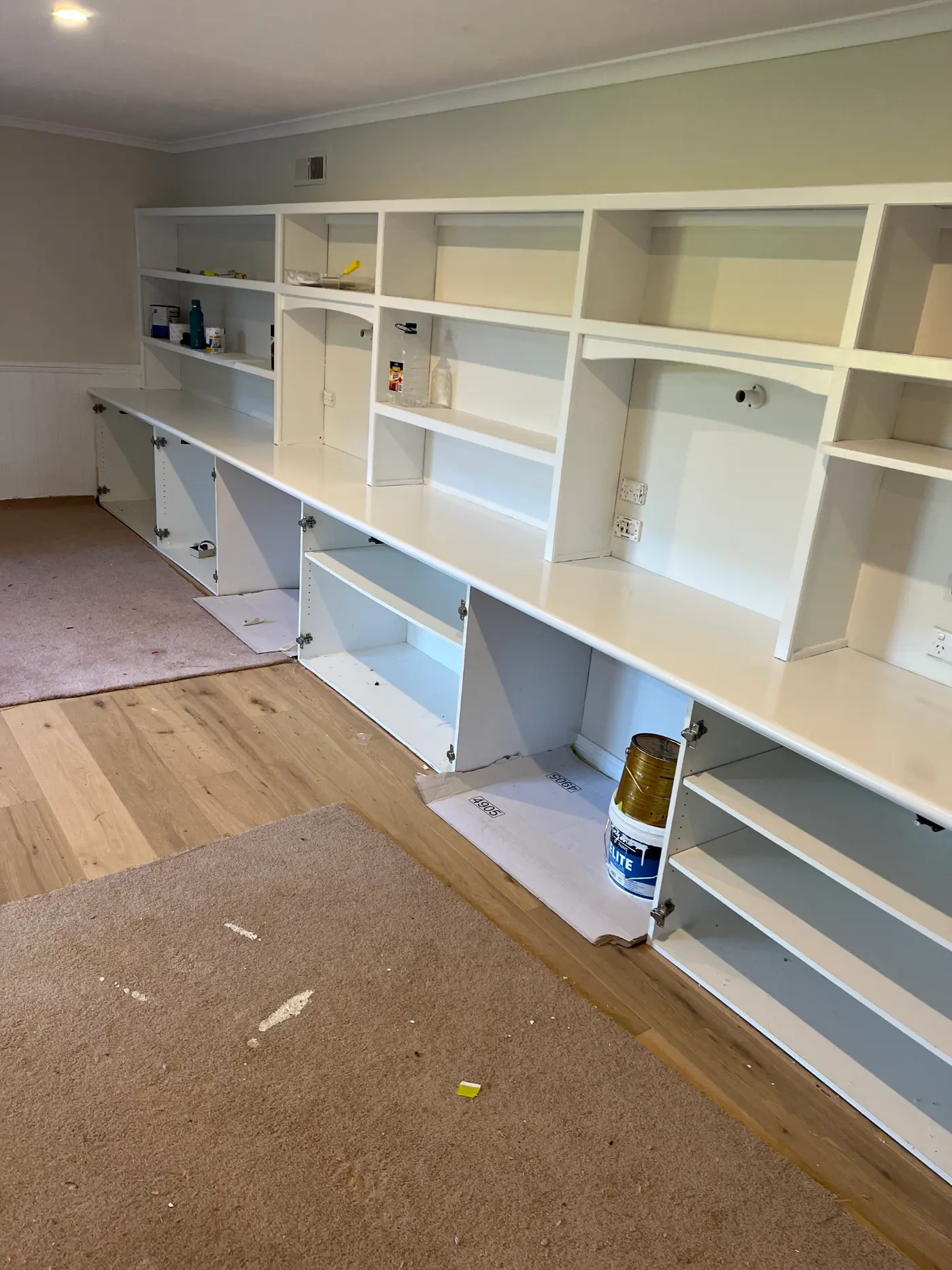 Long run of built-in wall shelving and cabinetry in a Dromana home mid-repaint, with cabinet doors open and a paint tin and drop sheet on the floor
