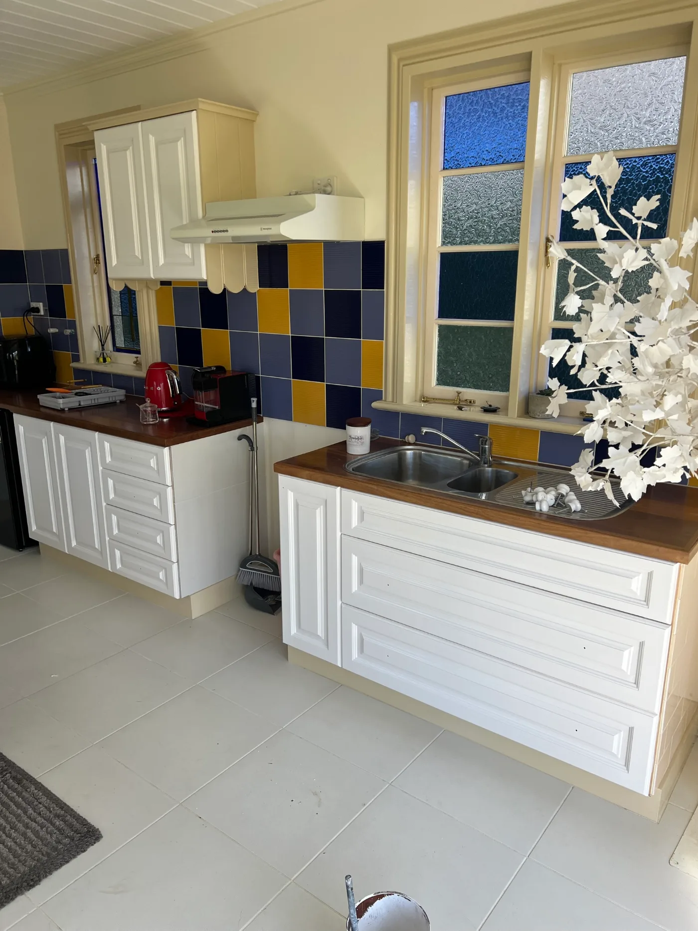 Wider view of a Dromana kitchen before resurfacing, showing a leadlight window, blue and gold tile splashback and white cabinetry along two benches