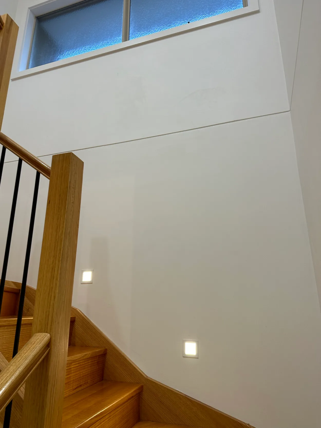 Stairwell in an Elsternwick home after interior painting, with white walls rising to a highlight window above natural timber stairs, newel post and handrail