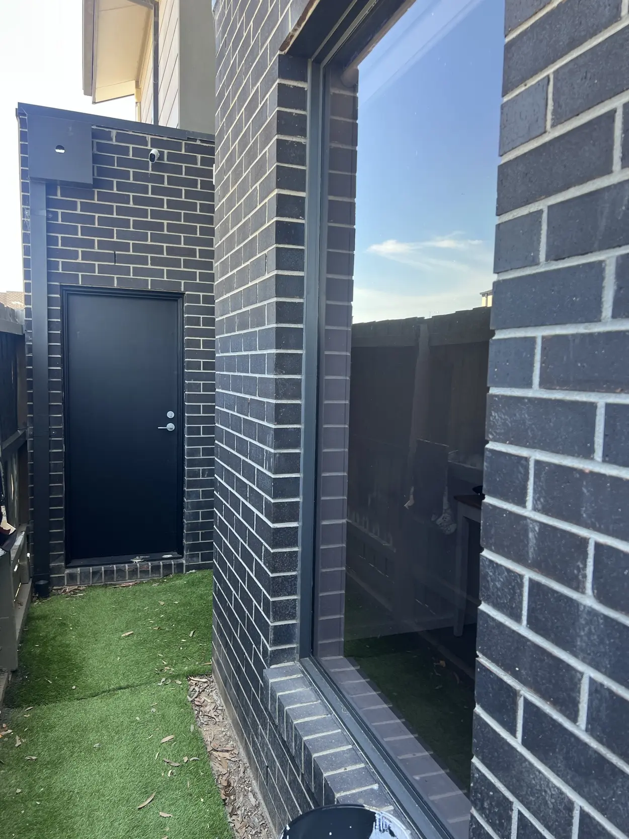 Dark face-brick exterior with a black door, black downpipe and meter box, and a large black-framed window