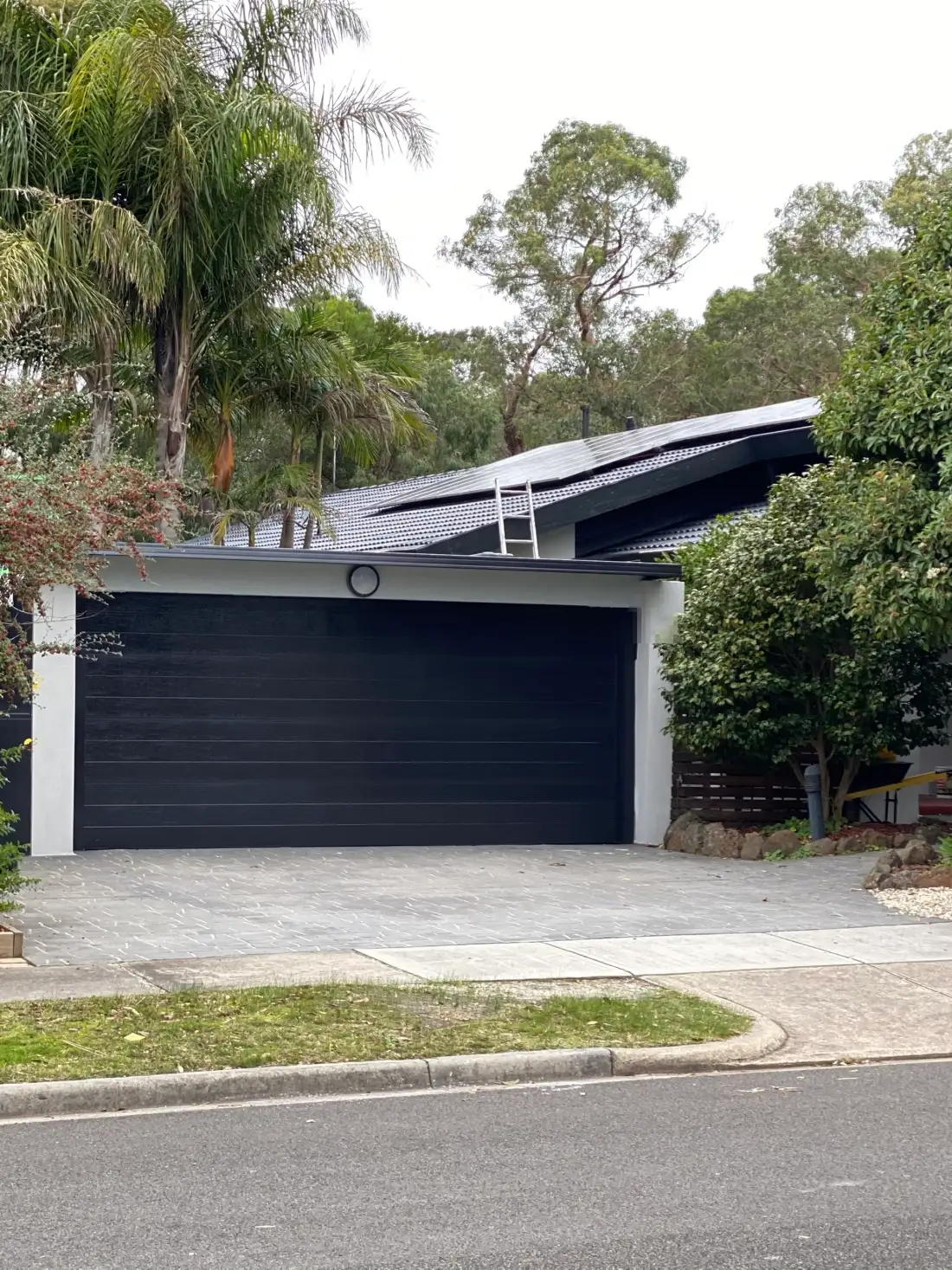 Street frontage of a Frankston South home after painting, with a wide charcoal garage door between white rendered piers under a dark fascia line