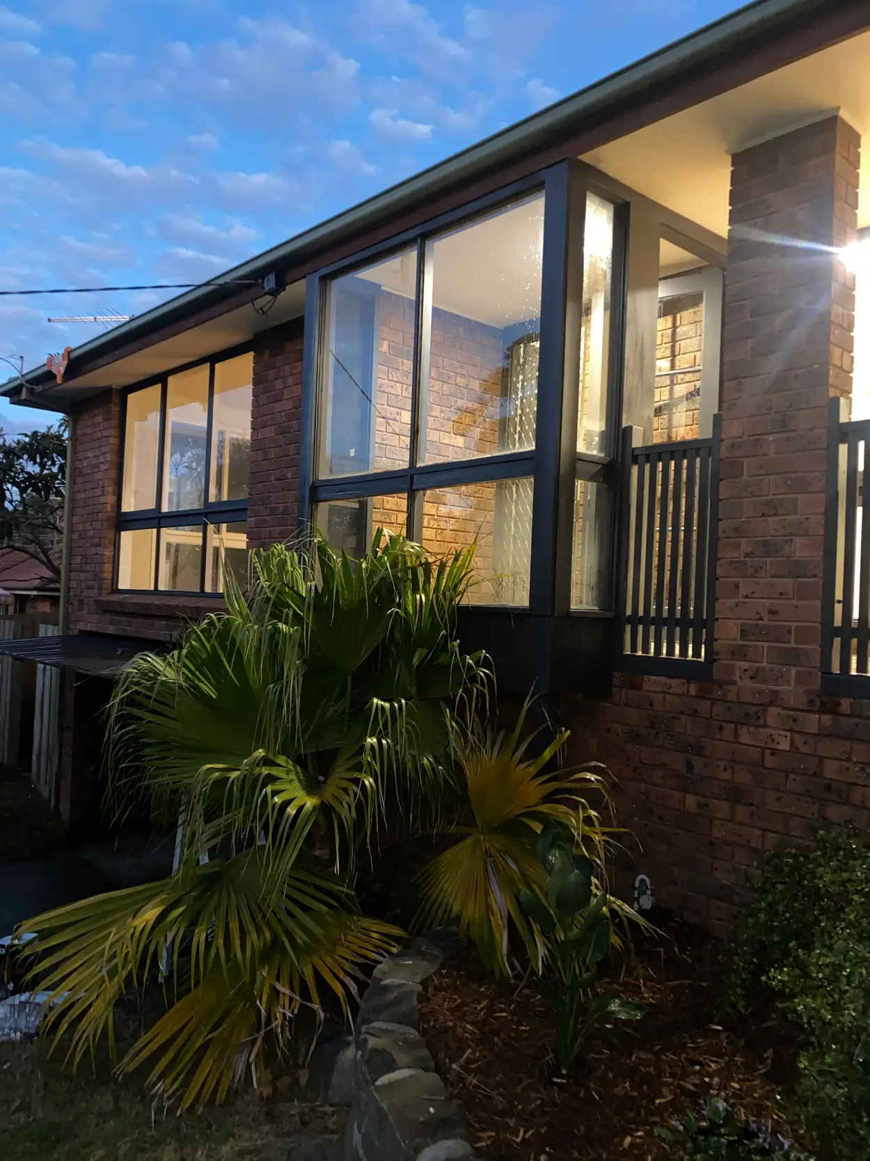Brick home in Frankston South after an exterior repaint, with charcoal window frames, mullions, eaves line and a slatted balustrade against the original brickwork