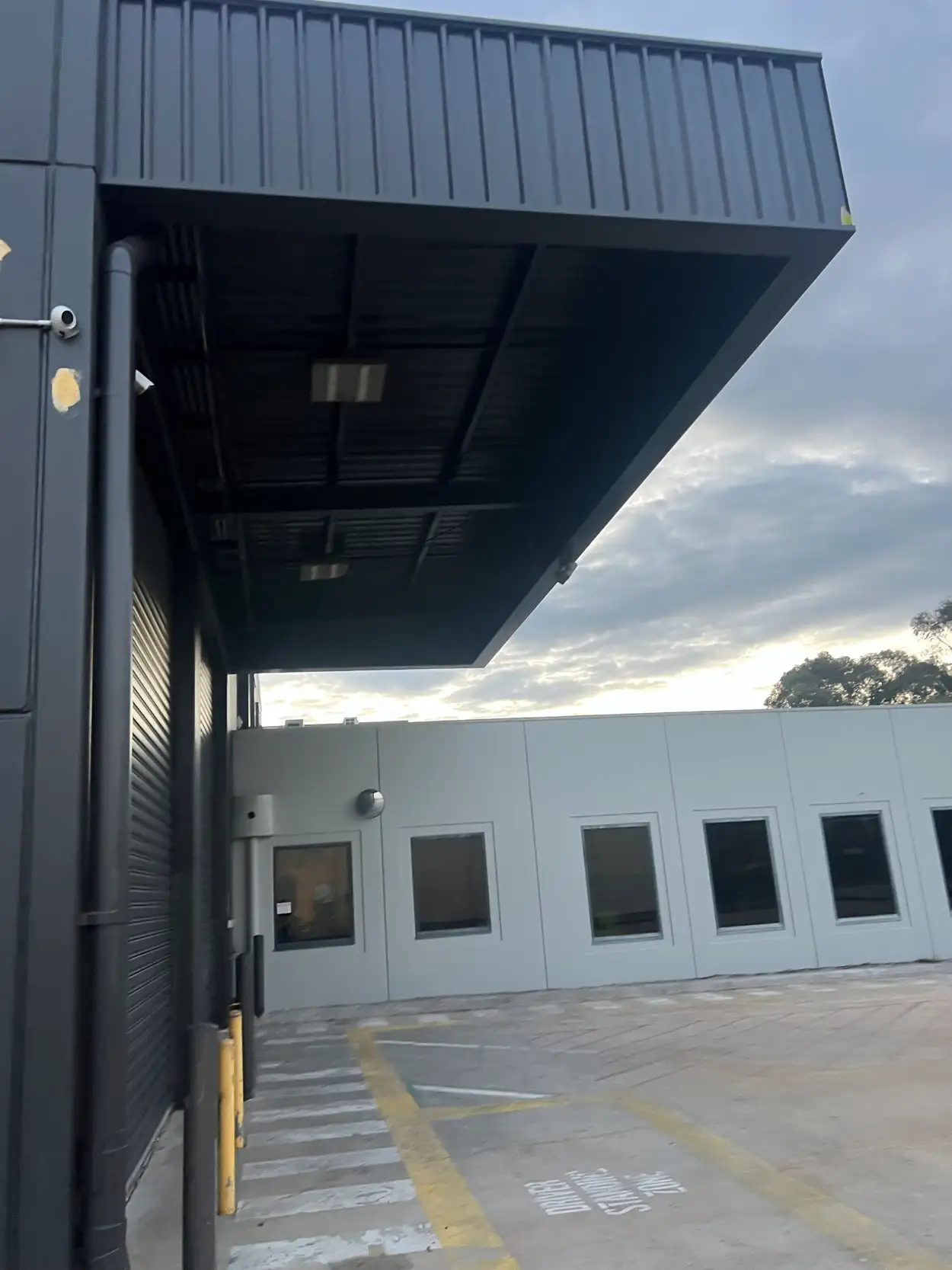 Charcoal loading-dock canopy, fascia and downpipe on a Heatherton warehouse, with the pale grey office block behind