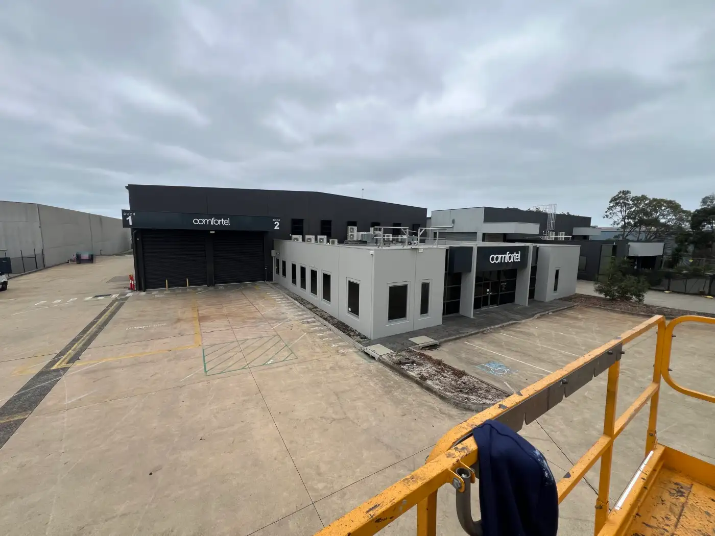 Commercial warehouse and office in Heatherton after exterior painting, with a pale grey office block in front of charcoal warehouse walls and roller doors