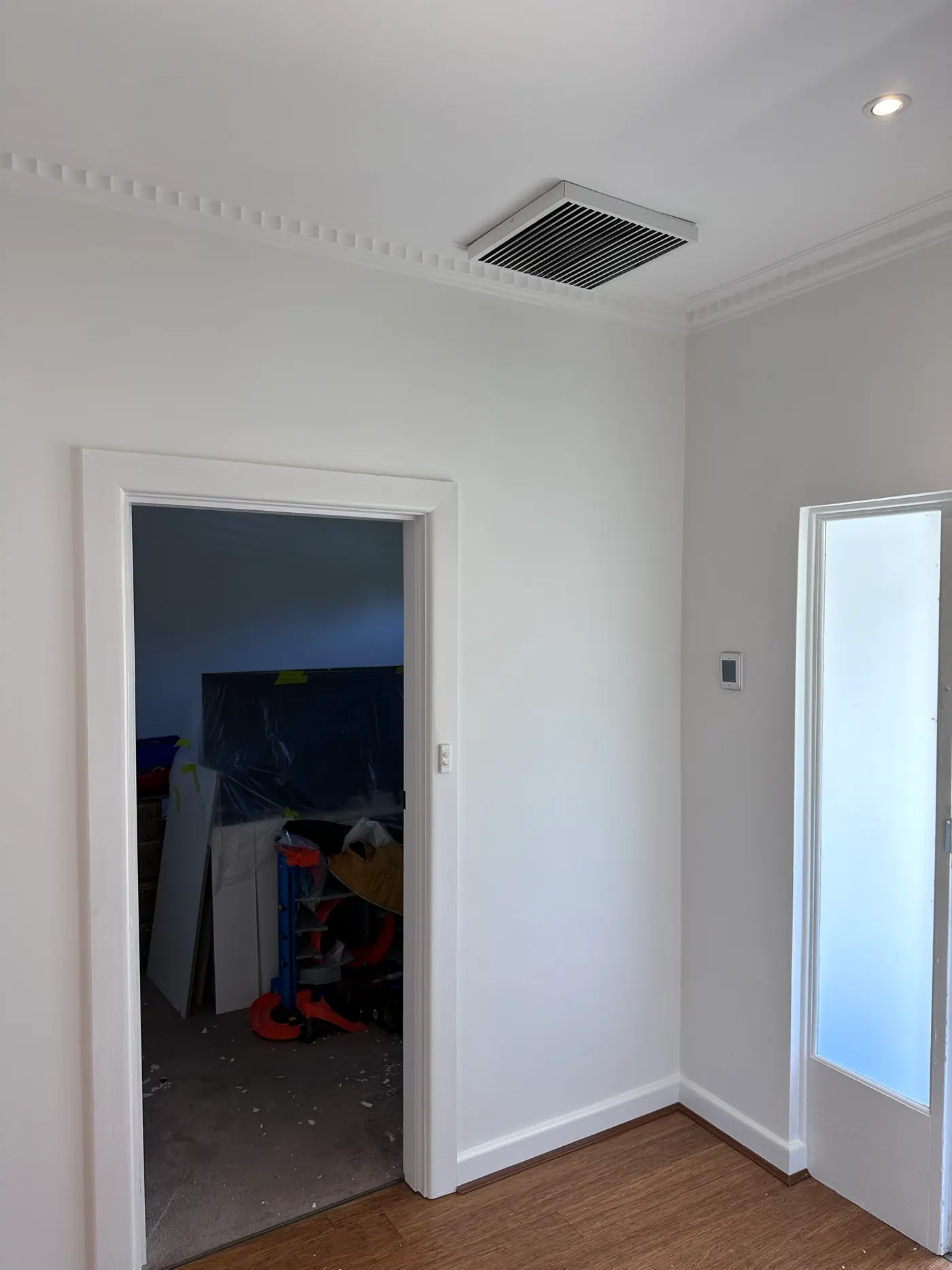 Corner of a room in a Highett home after repainting, with light grey walls, white cornice and skirting, and a doorway through to another room