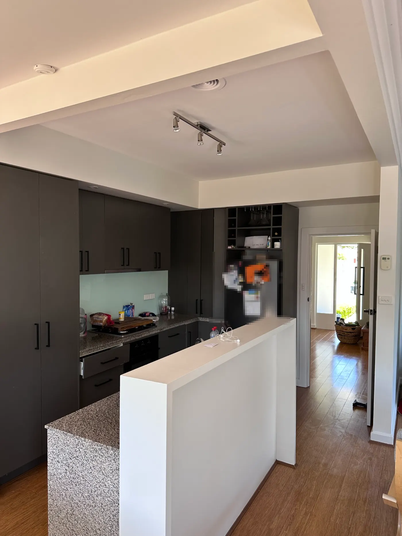 Kitchen and hallway in a Highett home after repainting, with white ceiling and walls above dark kitchen cabinetry and a timber-floored hallway leading to the front door