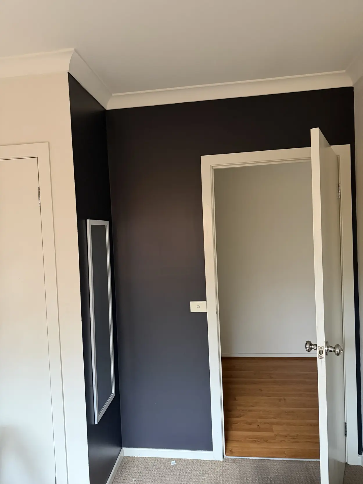 The same charcoal bedroom looking toward the door, with crisp white architraves, cornice and skirting against the dark walls