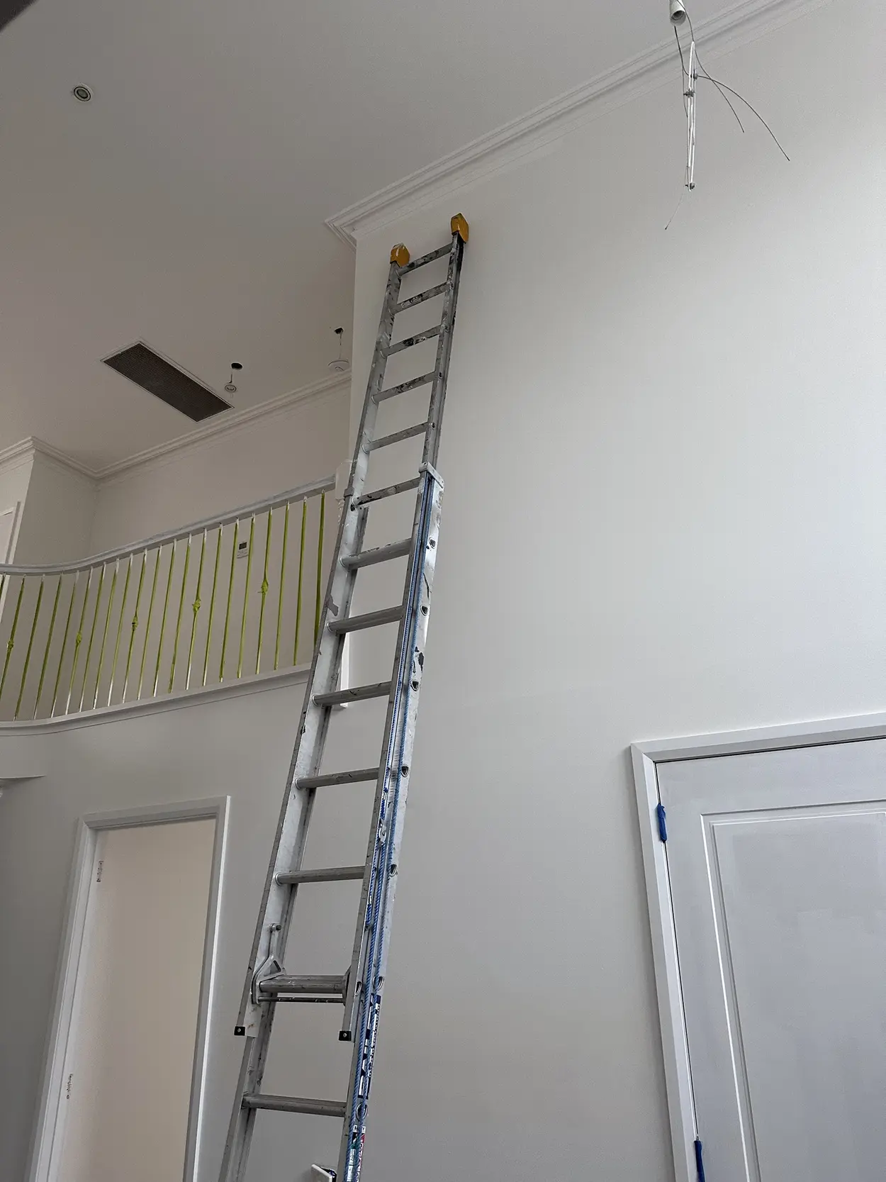 Double-height entry mid-repaint, with an extension ladder against the wall below the cornice and the curved upstairs balustrade wrapped in tape