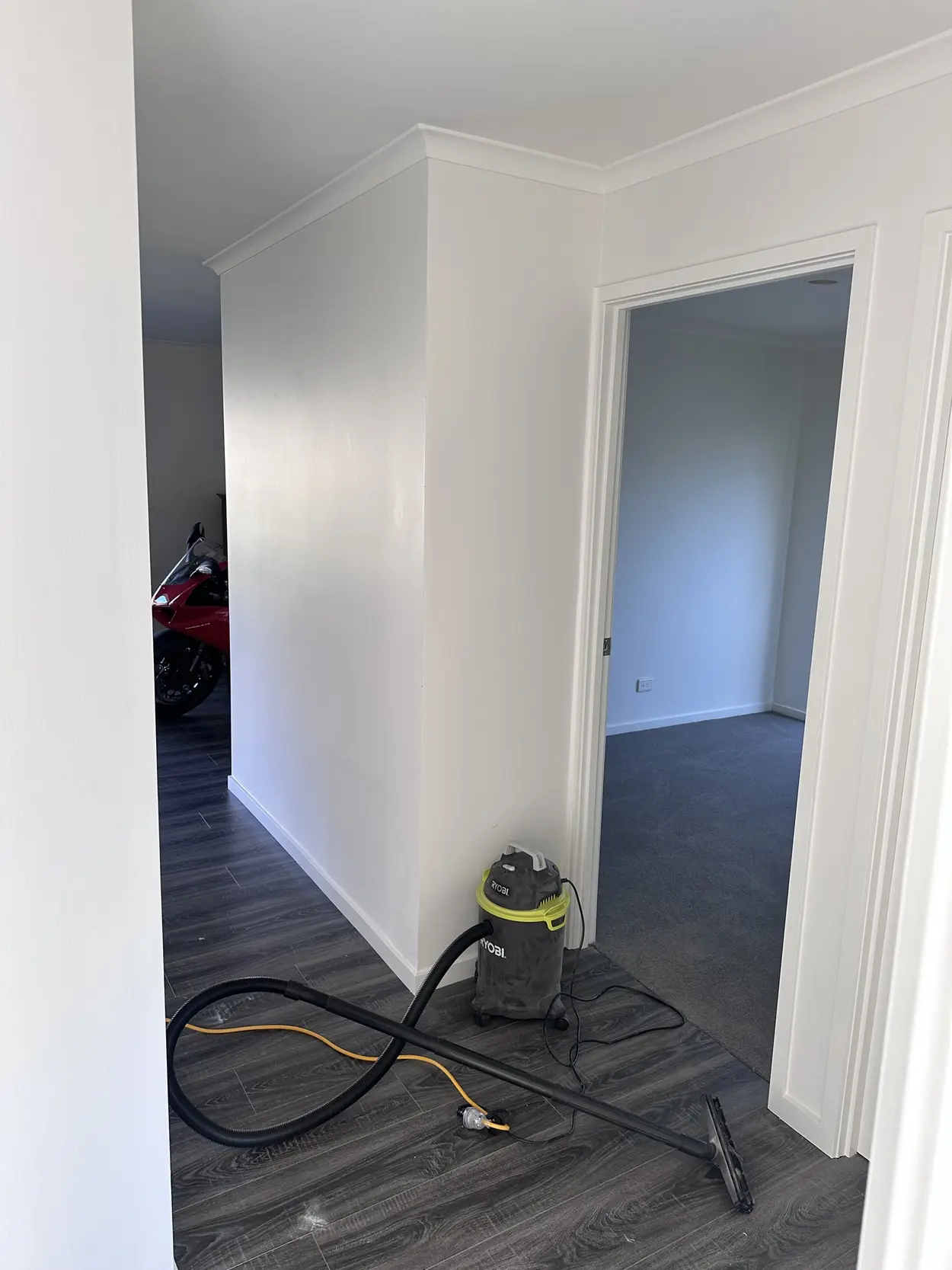 Finished hallway in white with crisp cornice, skirting and door frames, looking through to a carpeted bedroom