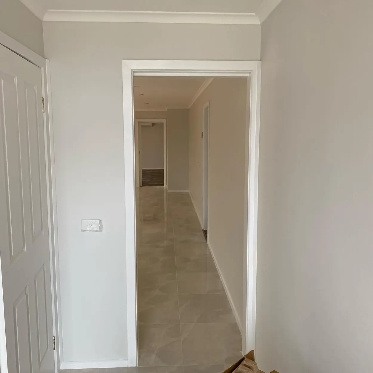 Finished hallway with soft grey walls, white door frames, skirting and cornice, and a polished tiled floor