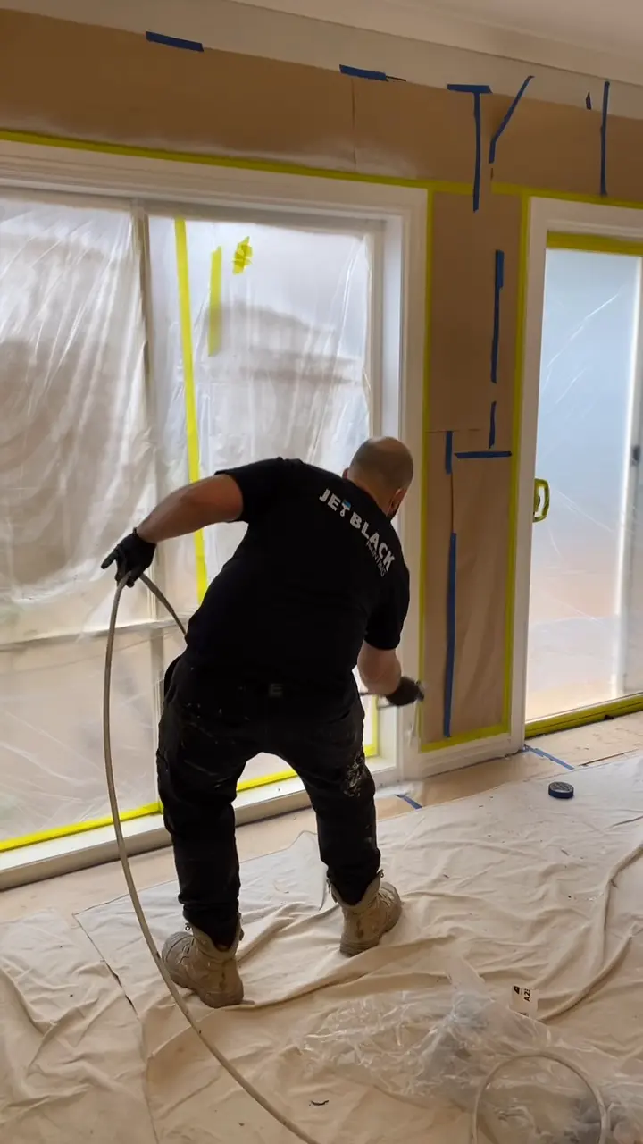 A Jetblack painter spraying around a set of sliding doors, with the glass covered in plastic and the walls masked with paper and tape