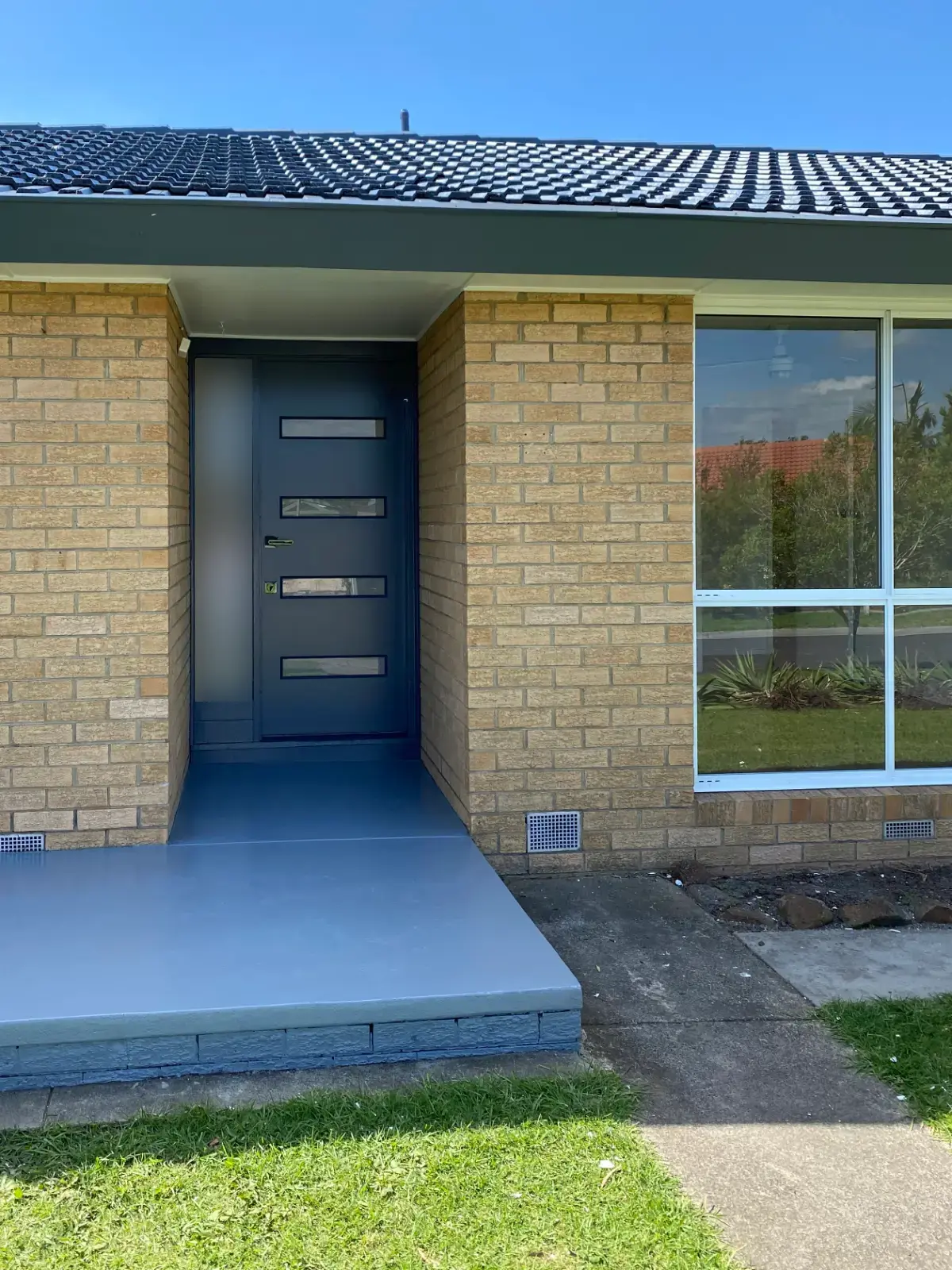 Entry of a Keysborough brick home after an exterior repaint, with a navy front door, dark grey fascia and gutter, a black tile roof and a repainted porch slab
