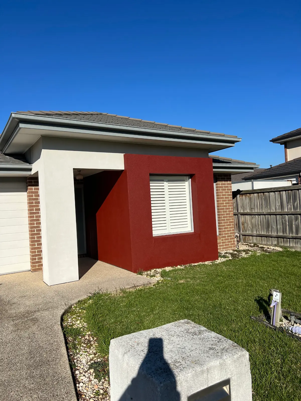 Entry of a single-storey Keysborough home after painting, with an off-white rendered portico column beside a deep terracotta-red feature wall and unpainted brick to either side