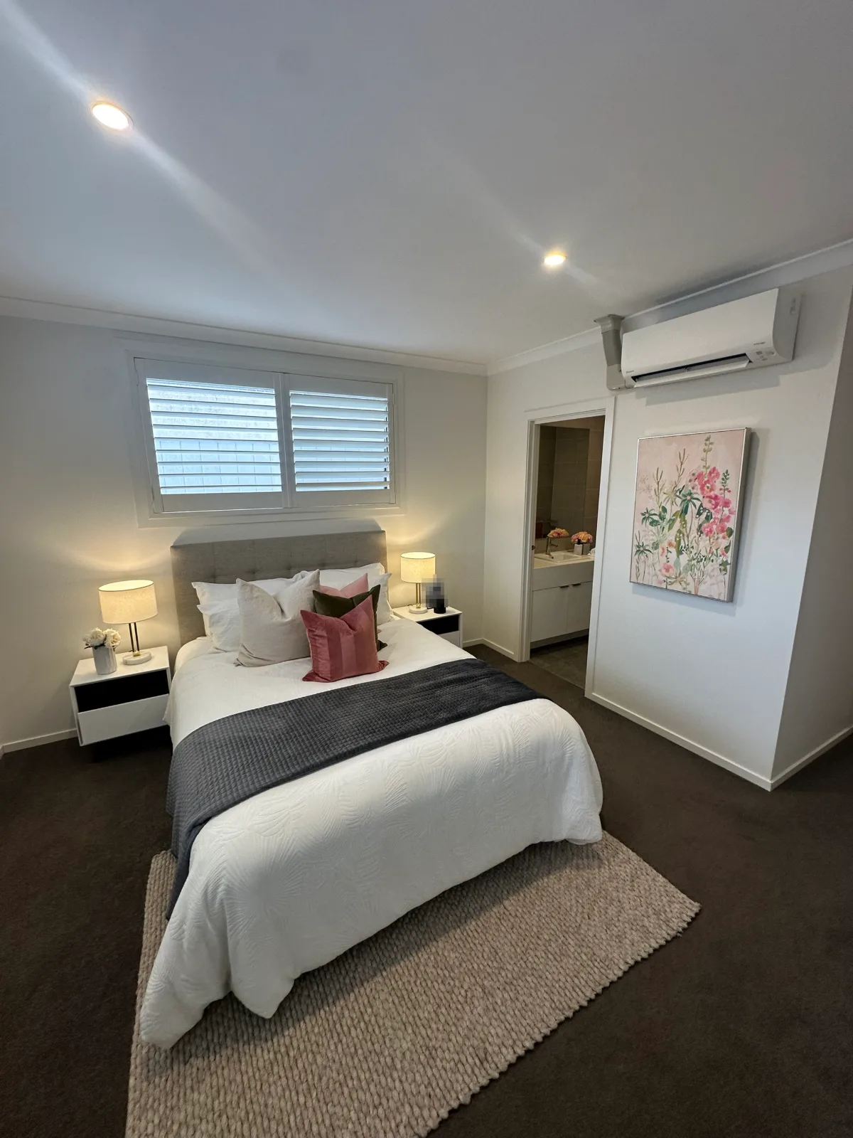 Main bedroom in a Keysborough home after interior painting, pale walls under a white ceiling with downlights, plantation shutters and an ensuite doorway