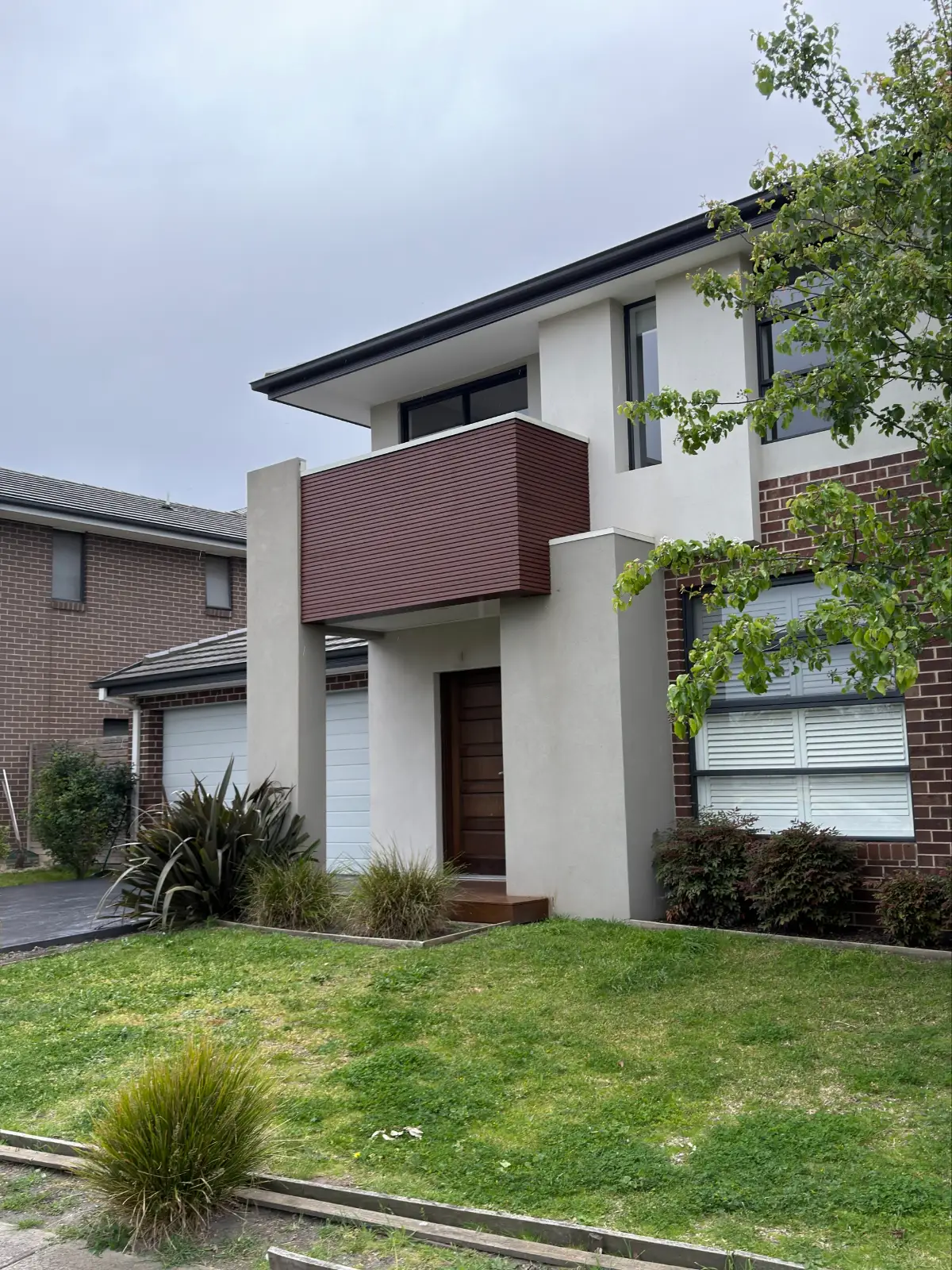 Two-storey brick and render home in Keysborough after painting, with pale grey render, a deep red-brown clad box beneath the upper balcony, charcoal window frames and the brickwork left unpainted